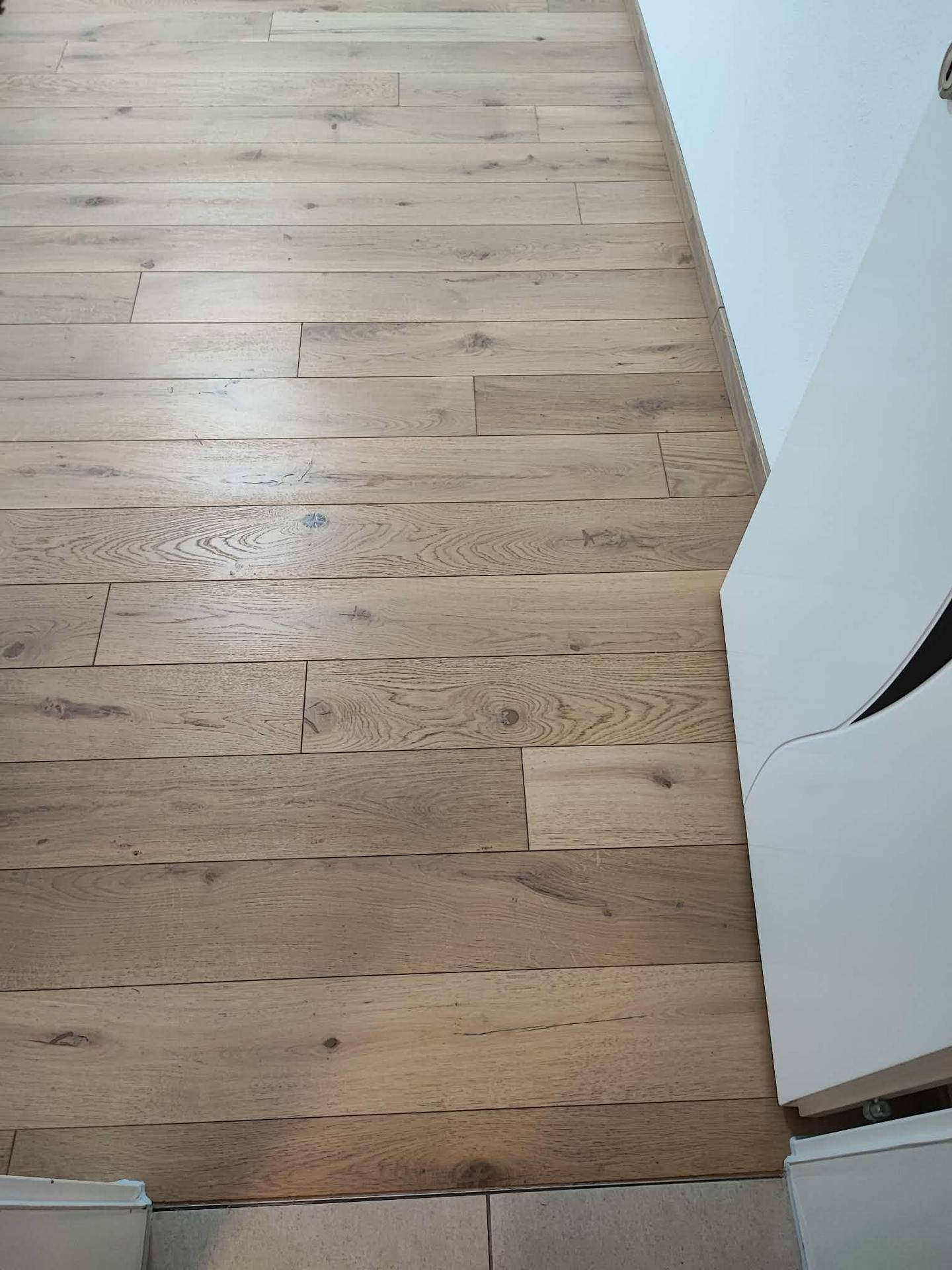 Heller Holzplankenboden im Flur, der zu einem gefliesten Bereich übergeht.