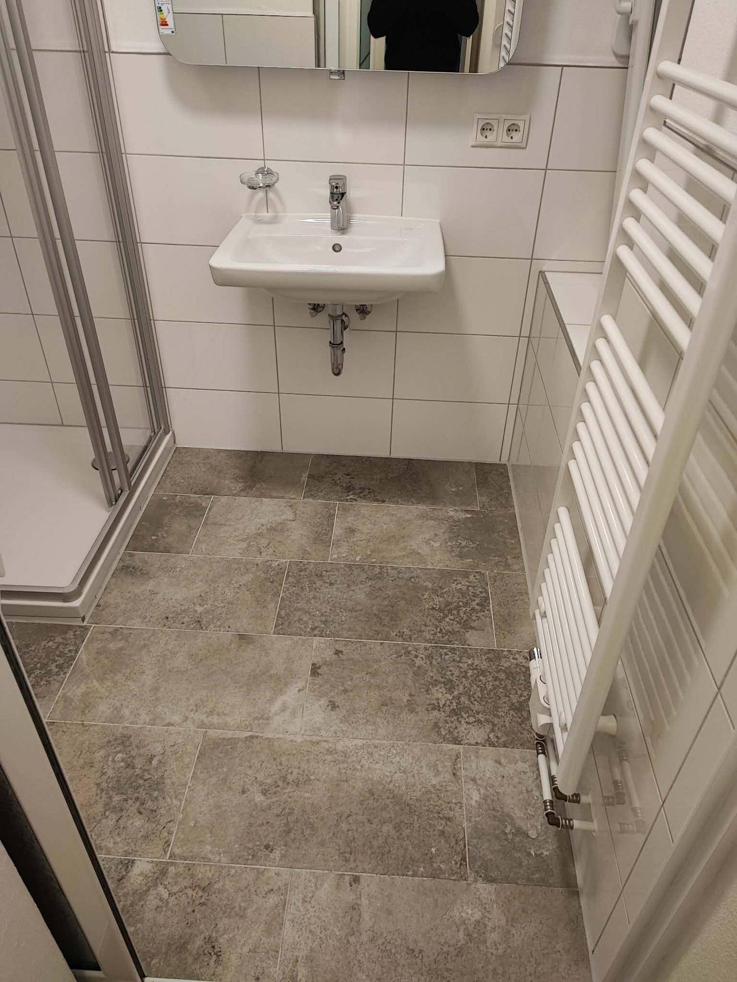 Badezimmer mit Waschbecken, Spiegel, beheiztem Handtuchhalter und Duschbereich.