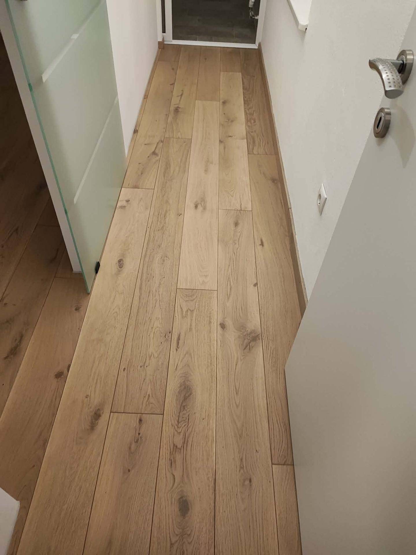 Detailansicht eines hellen Holzplankenbodens, der den Flur der Wohnung prägt.