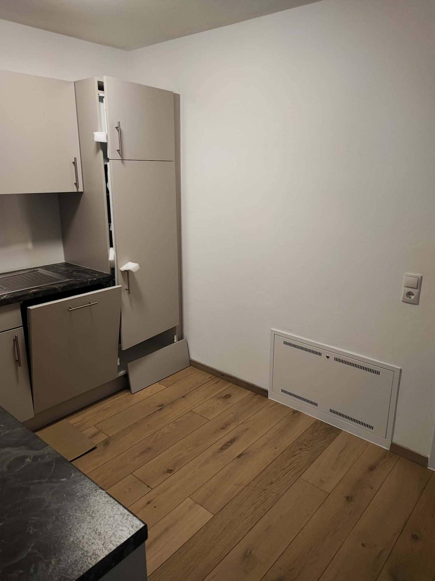 Küche mit hellgrauen Einbauschränken, dunkler Arbeitsplatte und integriertem Kühlschrank.