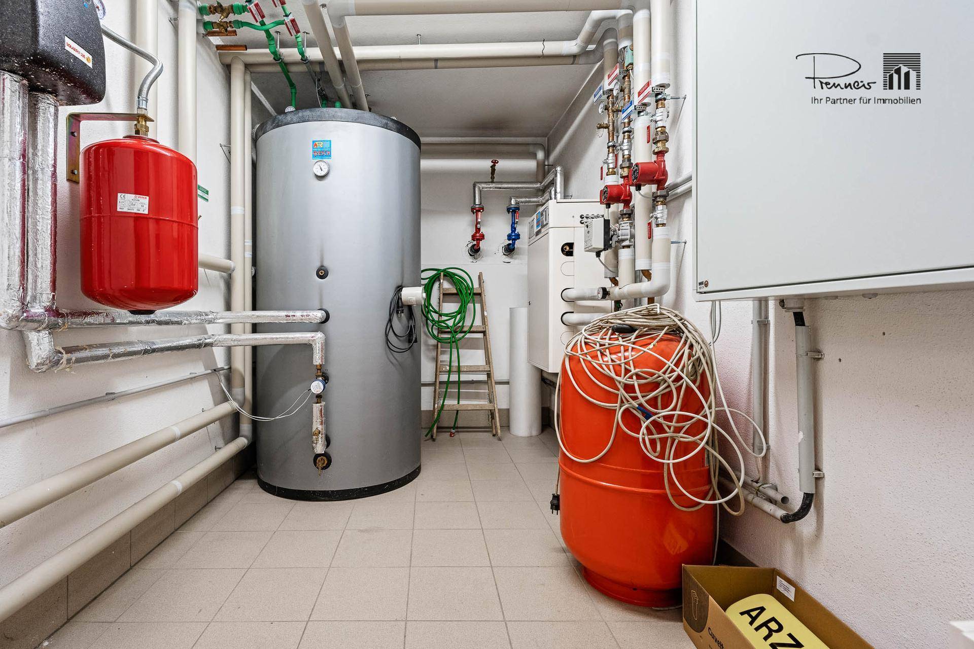 Technikraum mit Warmwasserspeichern, Heizungsanlagen und sichtbaren Rohrleitungen, alles ordentlich installiert.