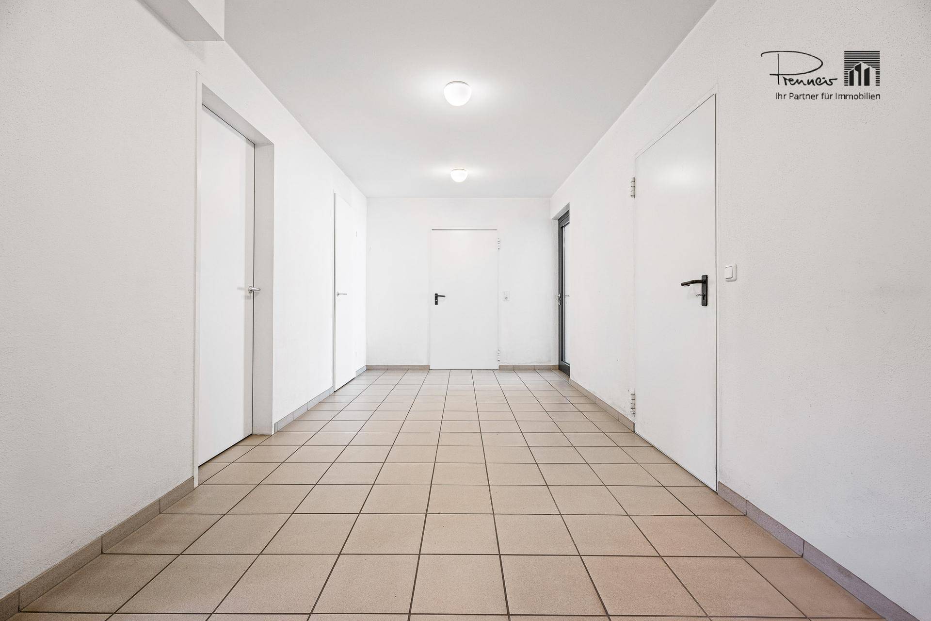 Heller Flur im Untergeschoss mit Fliesenboden und mehreren Türen, die zu verschiedenen Räumen führen.