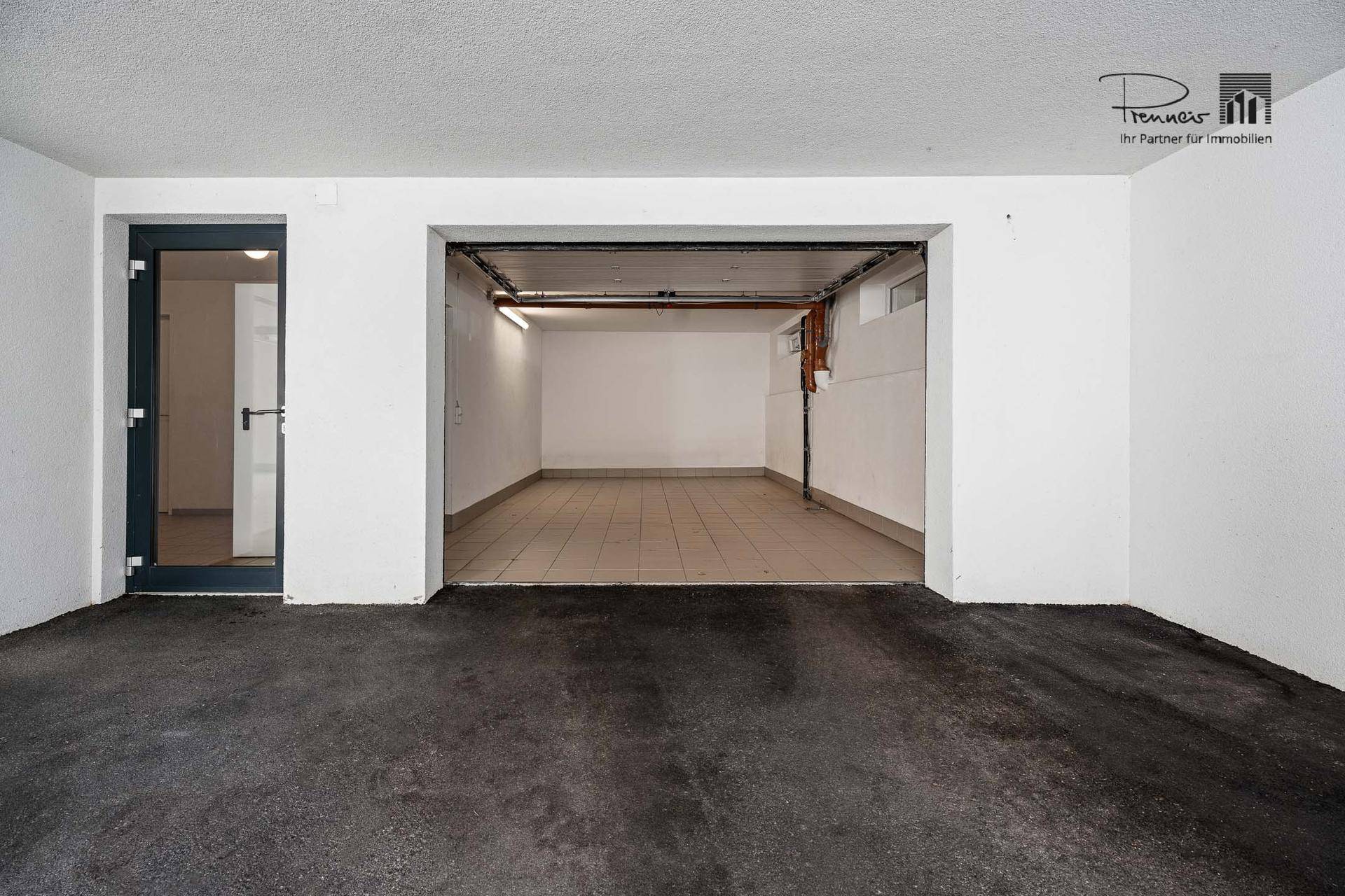 Garageneinfahrt mit einem offenen Tor und einer seitlichen Tür, die in den Innenbereich führt.