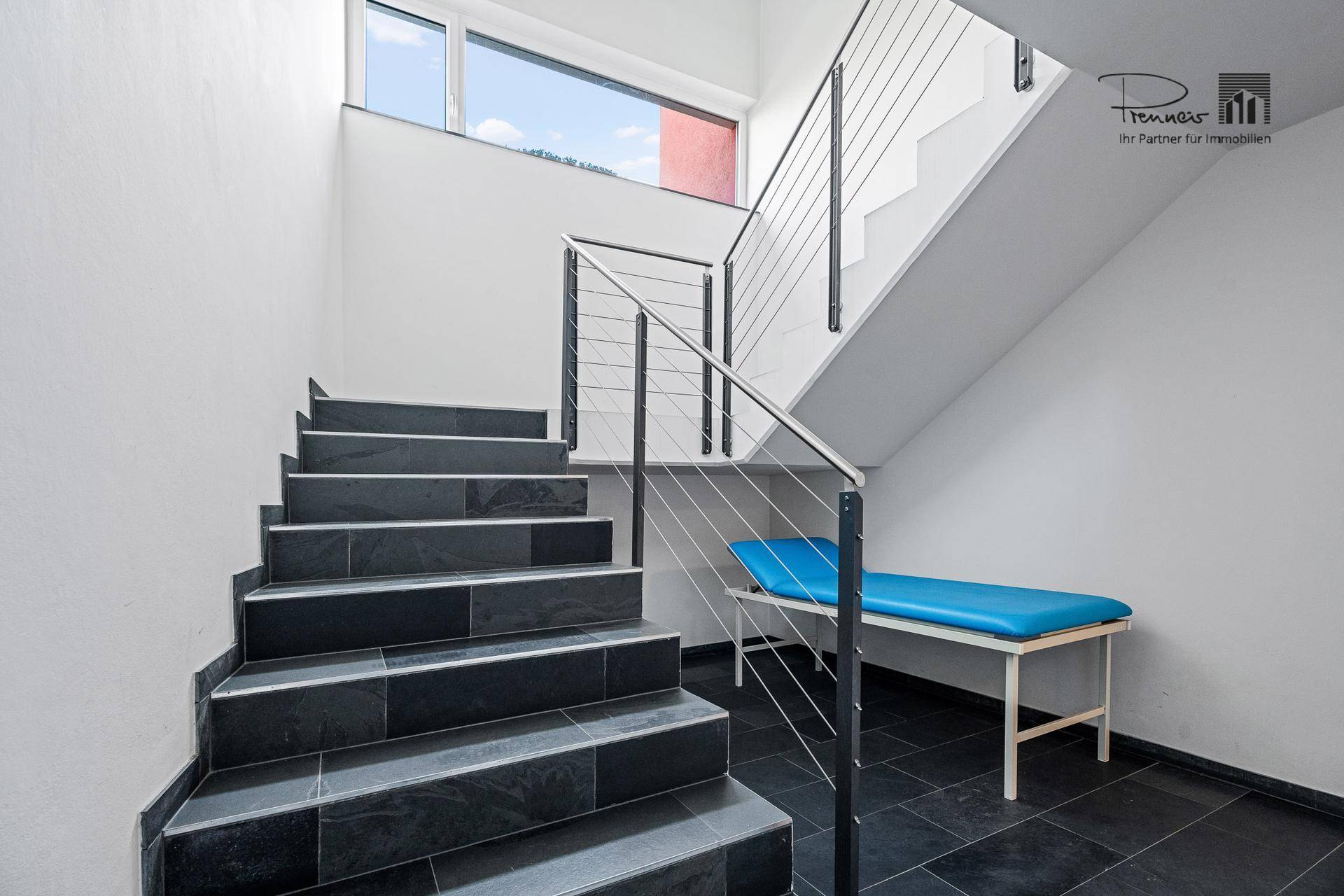 Modernes Treppenhaus mit dunklen Fliesenstufen und einem eleganten Edelstahlgeländer, das zu den oberen Etagen führt.