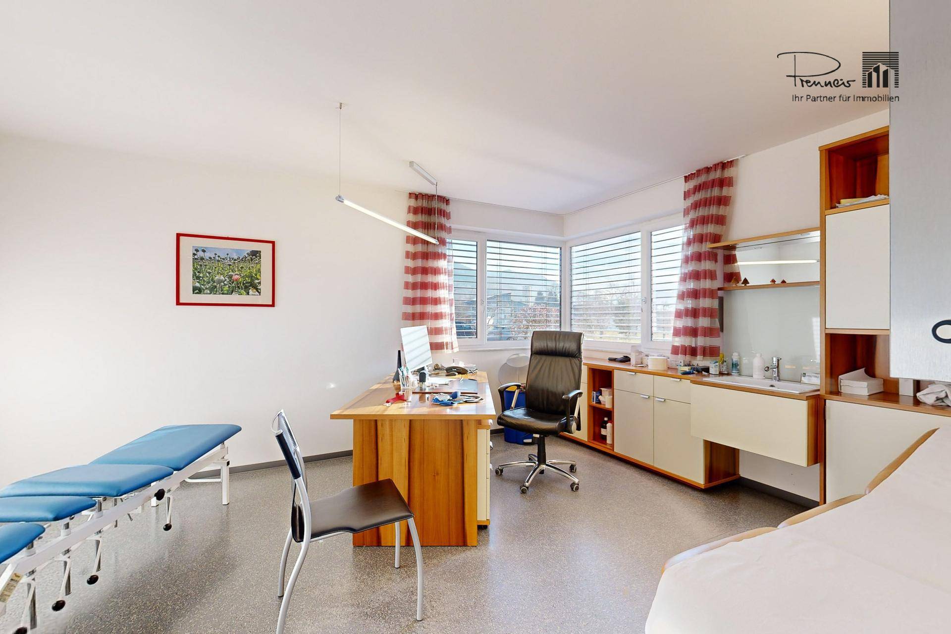 Helles Büro oder Behandlungszimmer mit großen Fenstern, modernem Schreibtisch und einer Untersuchungsliege.