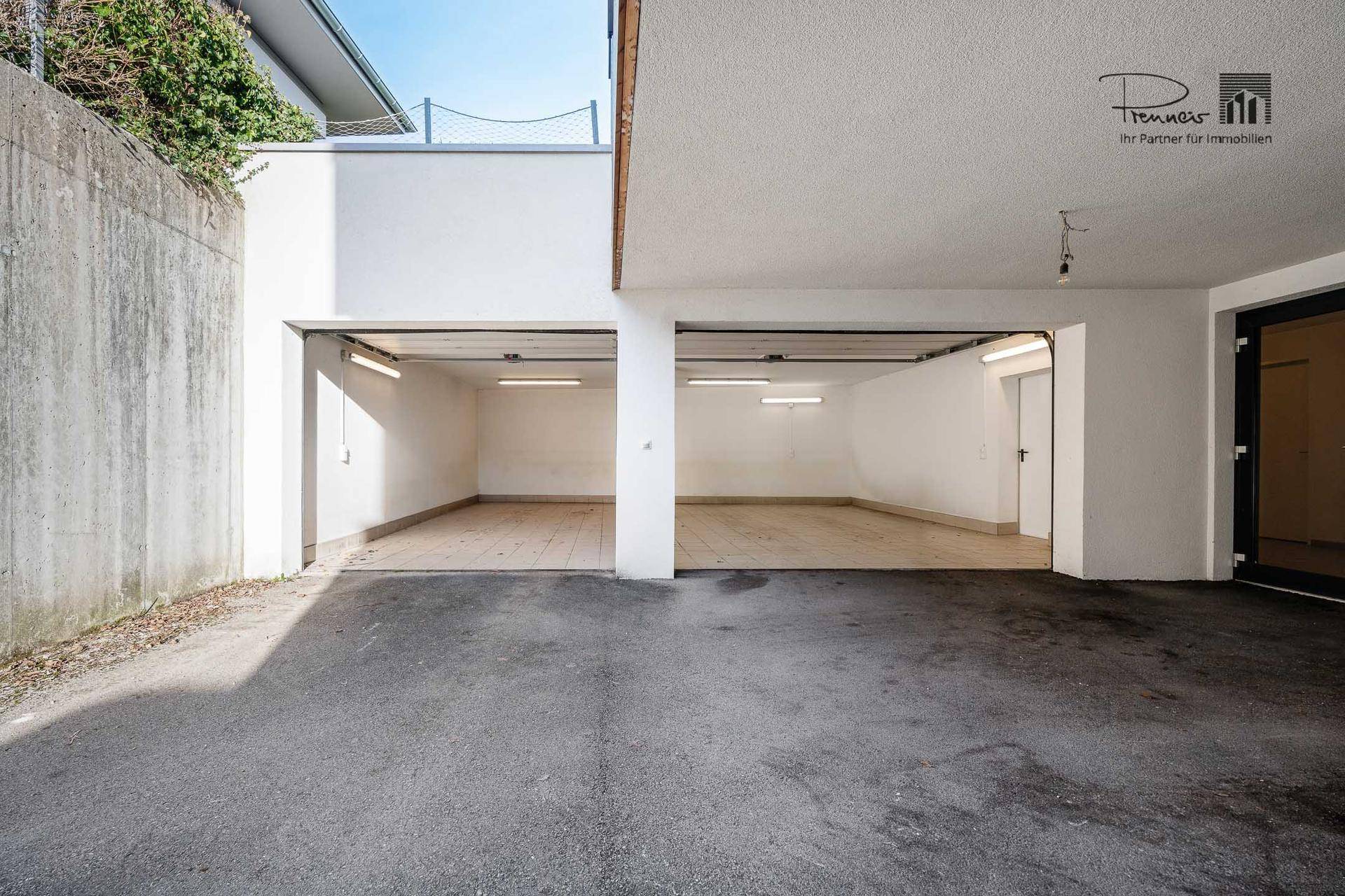 Einfahrt zu einer Doppelgarage im Untergeschoss mit zwei offenen Toren und einer Betonwand.