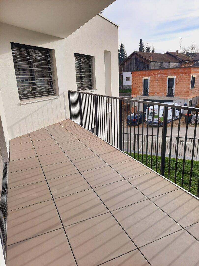 Geräumiger Balkon mit Fliesenboden und Blick auf die Nachbarschaft und ein im Bau befindliches Haus.