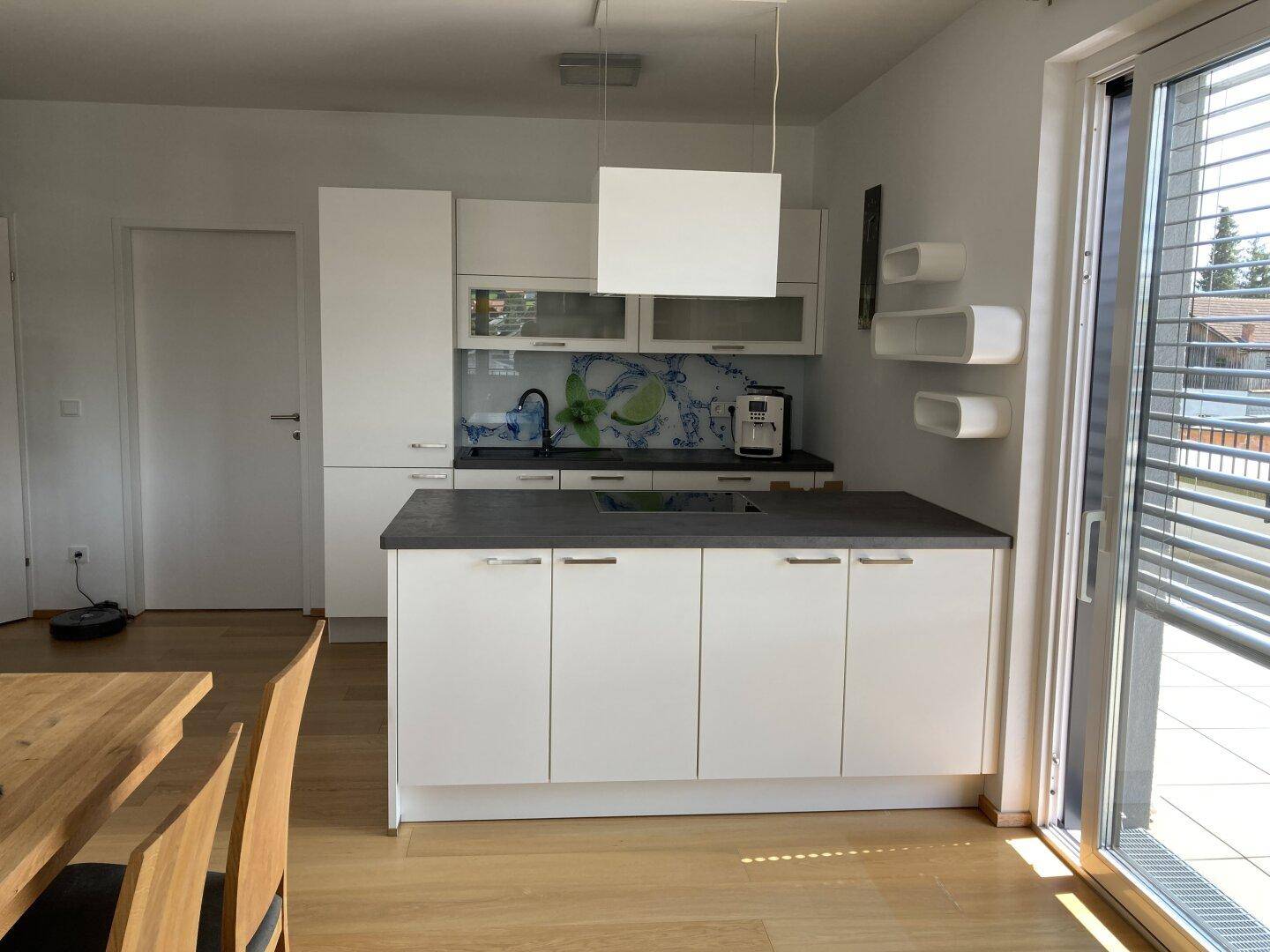 Moderne Einbauküche mit Kochinsel, weißen Schränken und Zugang zu einem sonnigen Balkon.