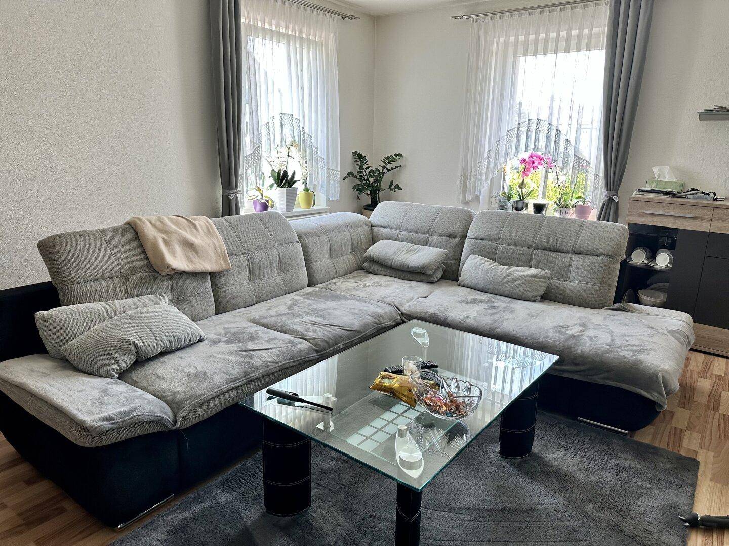 Helles Wohnzimmer mit großer Eckcouch und Fenstern, die viel Tageslicht hereinlassen.