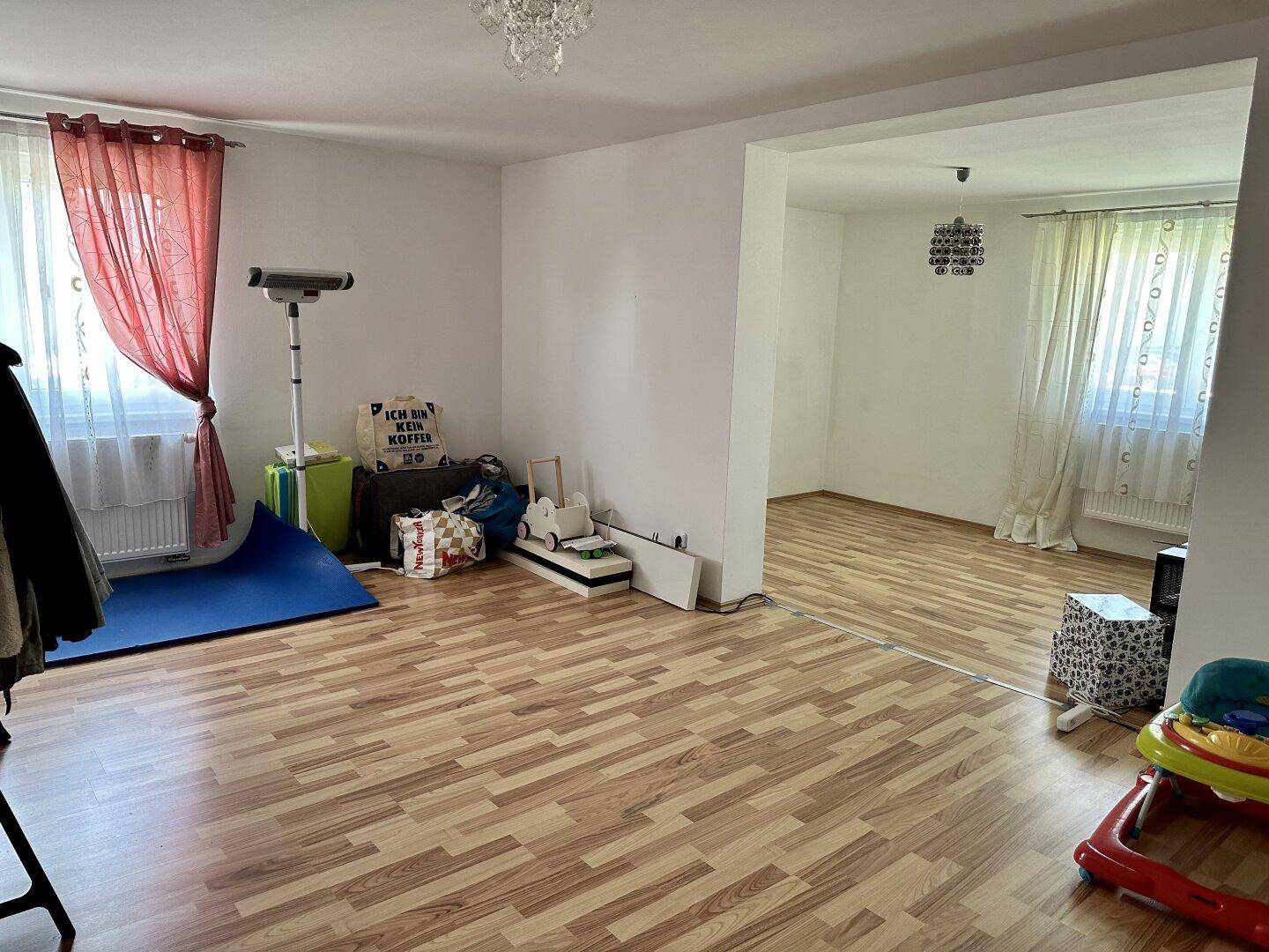 Leerer Raum mit Laminatboden und Fenstern, die für ausreichend Tageslicht sorgen.