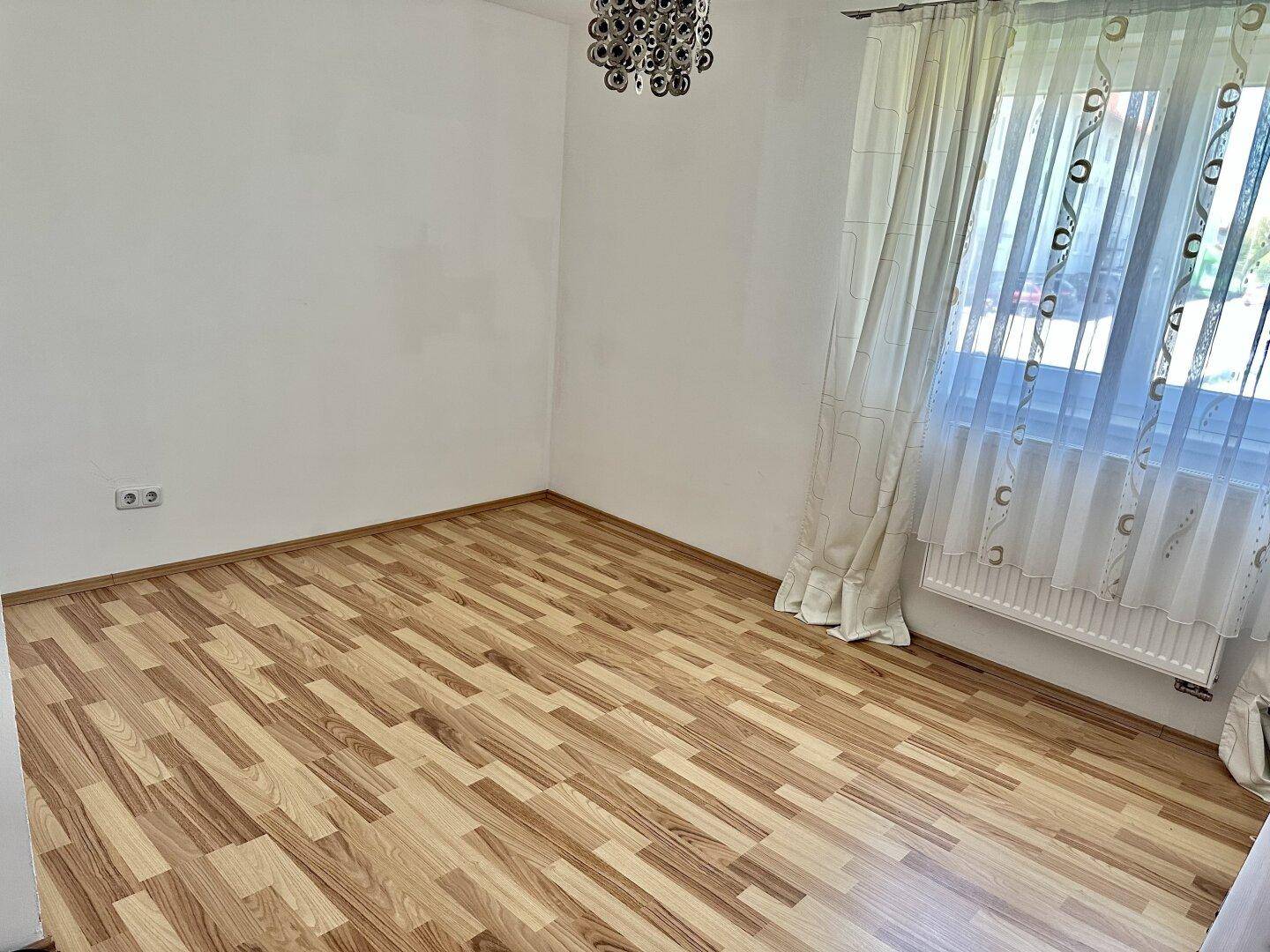 Heller, leerer Raum mit Laminatboden und einem großen Fenster für viel Lichteinfall.