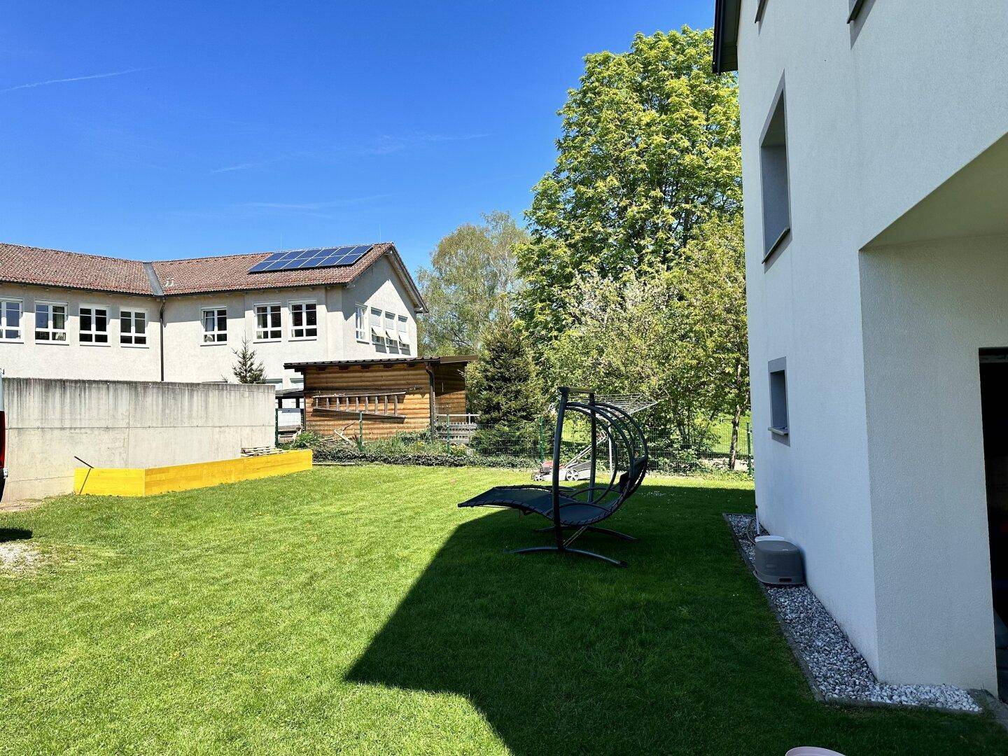 Ruhiger Gartenbereich mit Rasenfläche und einer modernen Outdoor-Sitzgelegenheit zum Entspannen.