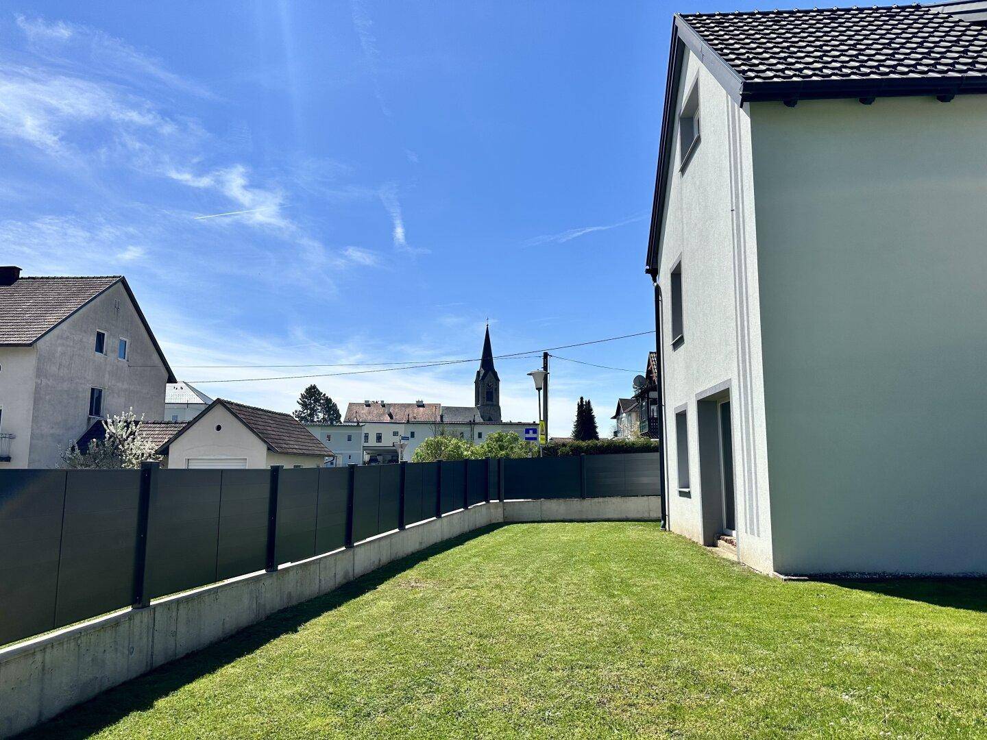 Gartenbereich mit Rasenfläche und Blick auf die Nachbarschaft mit einem Kirchturm in der Ferne.