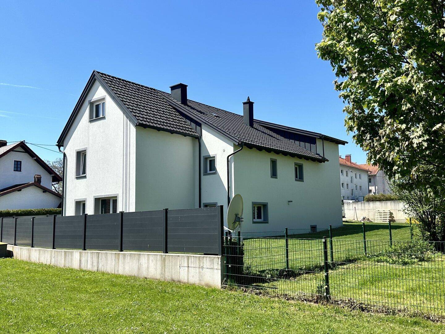 Seitenansicht des Wohnhauses mit Garten, Zaun und Blick auf die umliegende Bebauung.