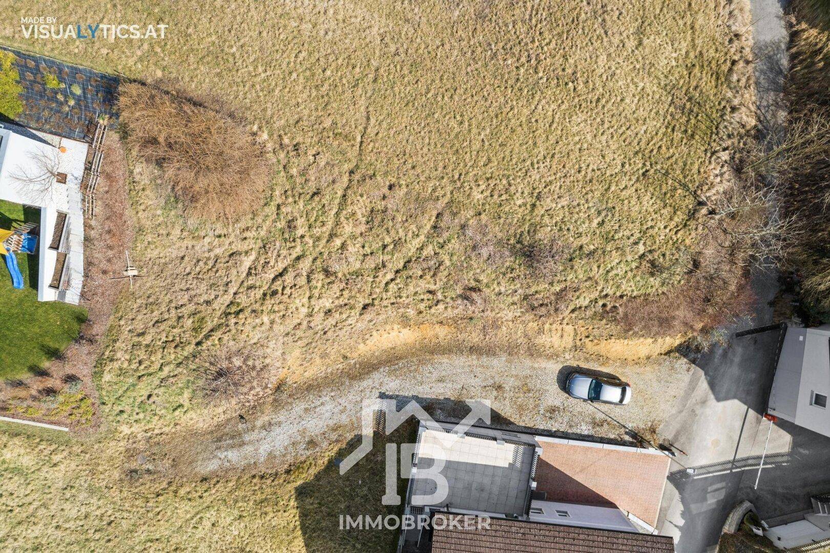 Vogelperspektive eines unbebauten Grundstücks mit angrenzenden Häusern und einem geparkten Auto.