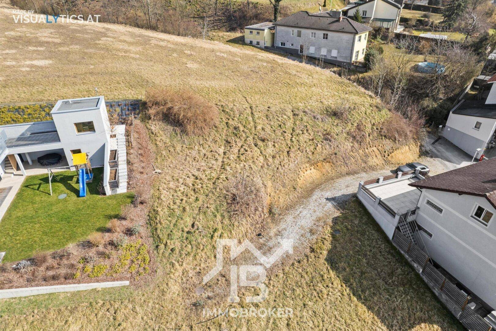 Luftaufnahme eines abfallenden Grundstücks mit einem modernen Haus und einem Kinderspielplatz.