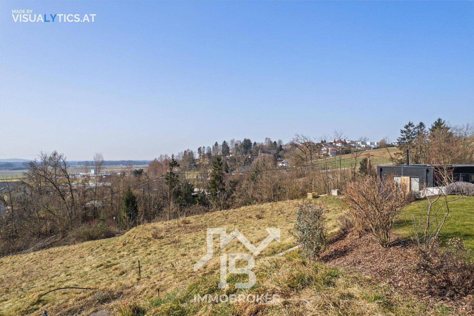 Hügeliges Gelände mit trockenem Gras und vereinzelten Bäumen, im Hintergrund eine ländliche Siedlung.