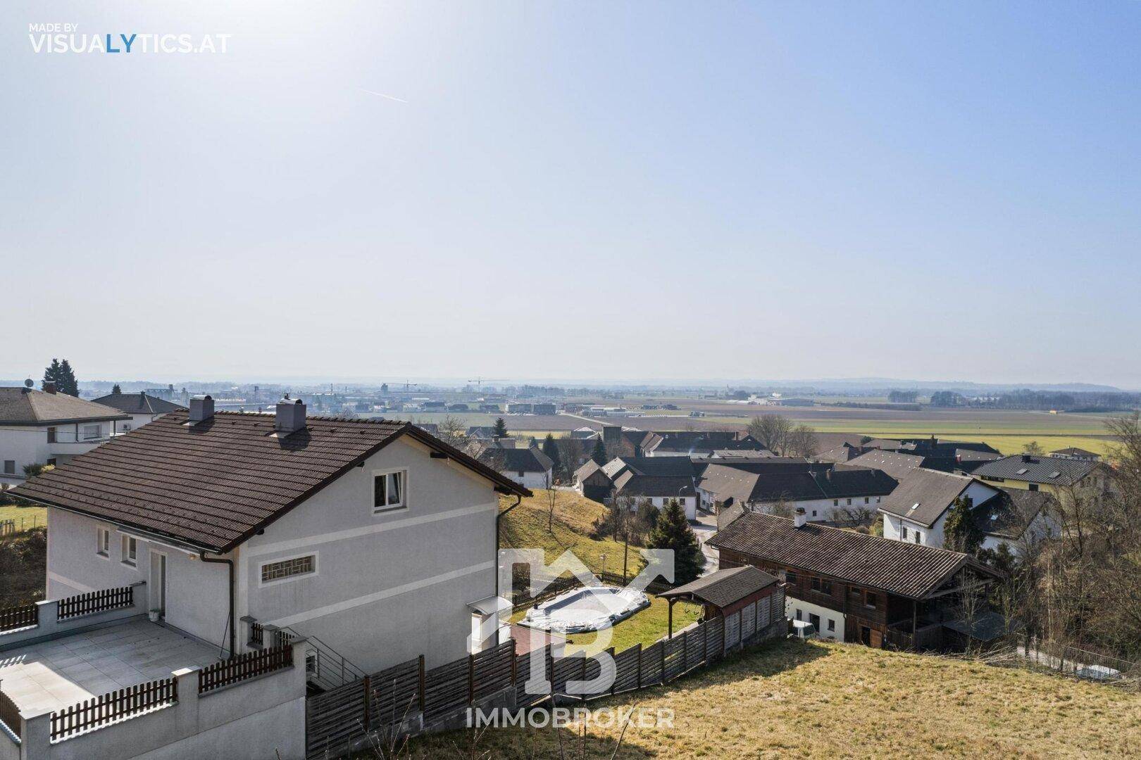 Wohnhaus mit großer Terrasse und einem abgedeckten Pool, umgeben von ländlicher Landschaft.