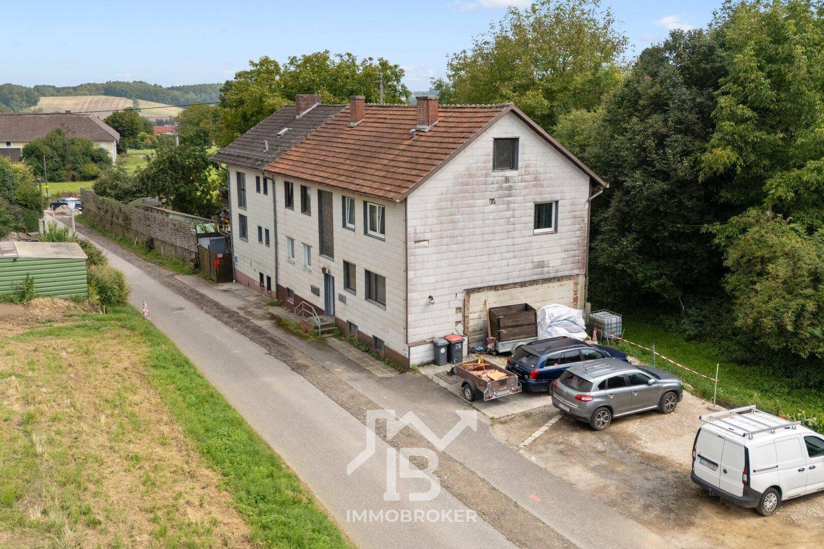 Luftaufnahme des Anwesens mit dem Mehrfamilienhaus, Parkplätzen und weiten Feldern im Hintergrund.