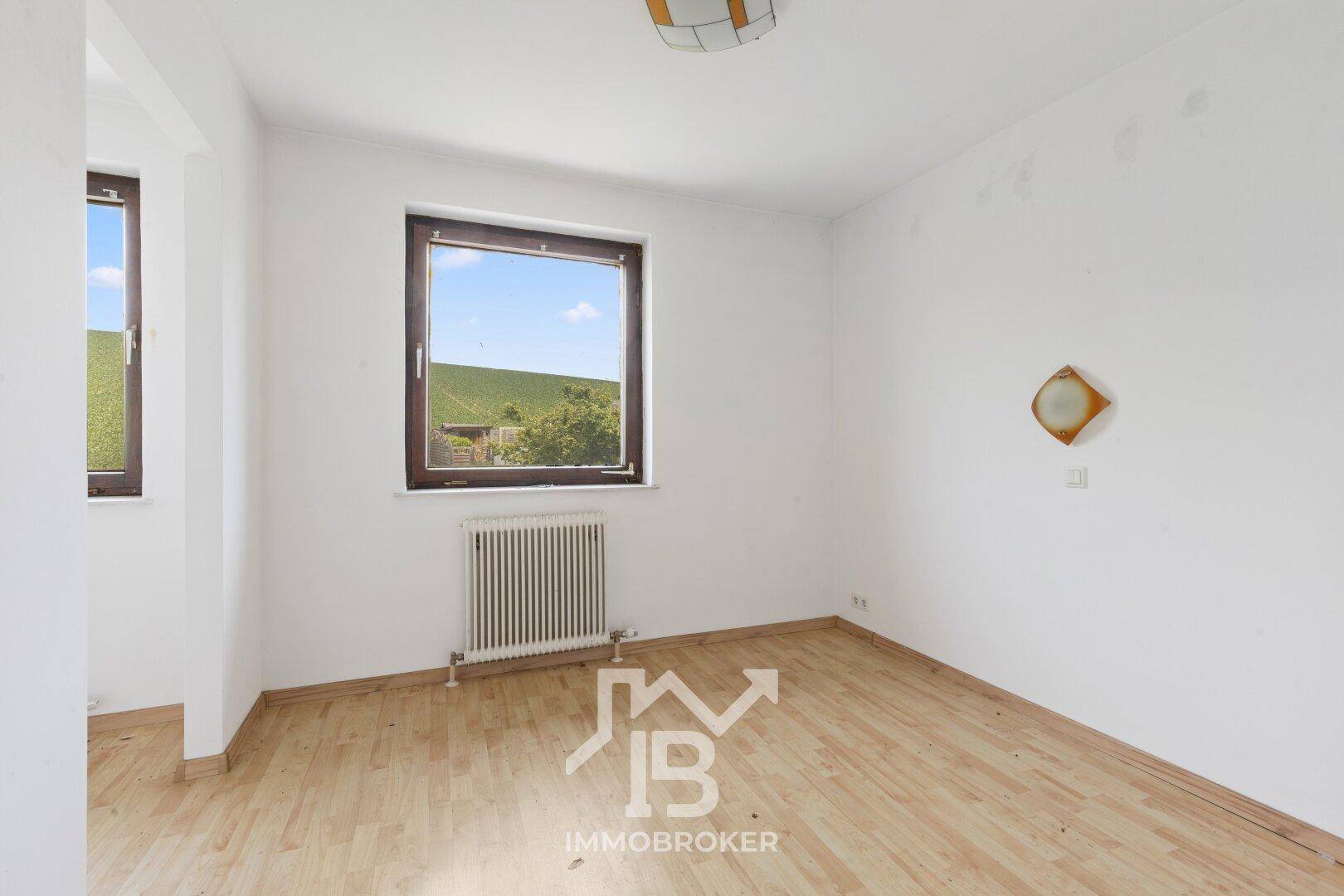 Heller Raum mit Laminatboden, einem großen Fenster und Blick ins Grüne.