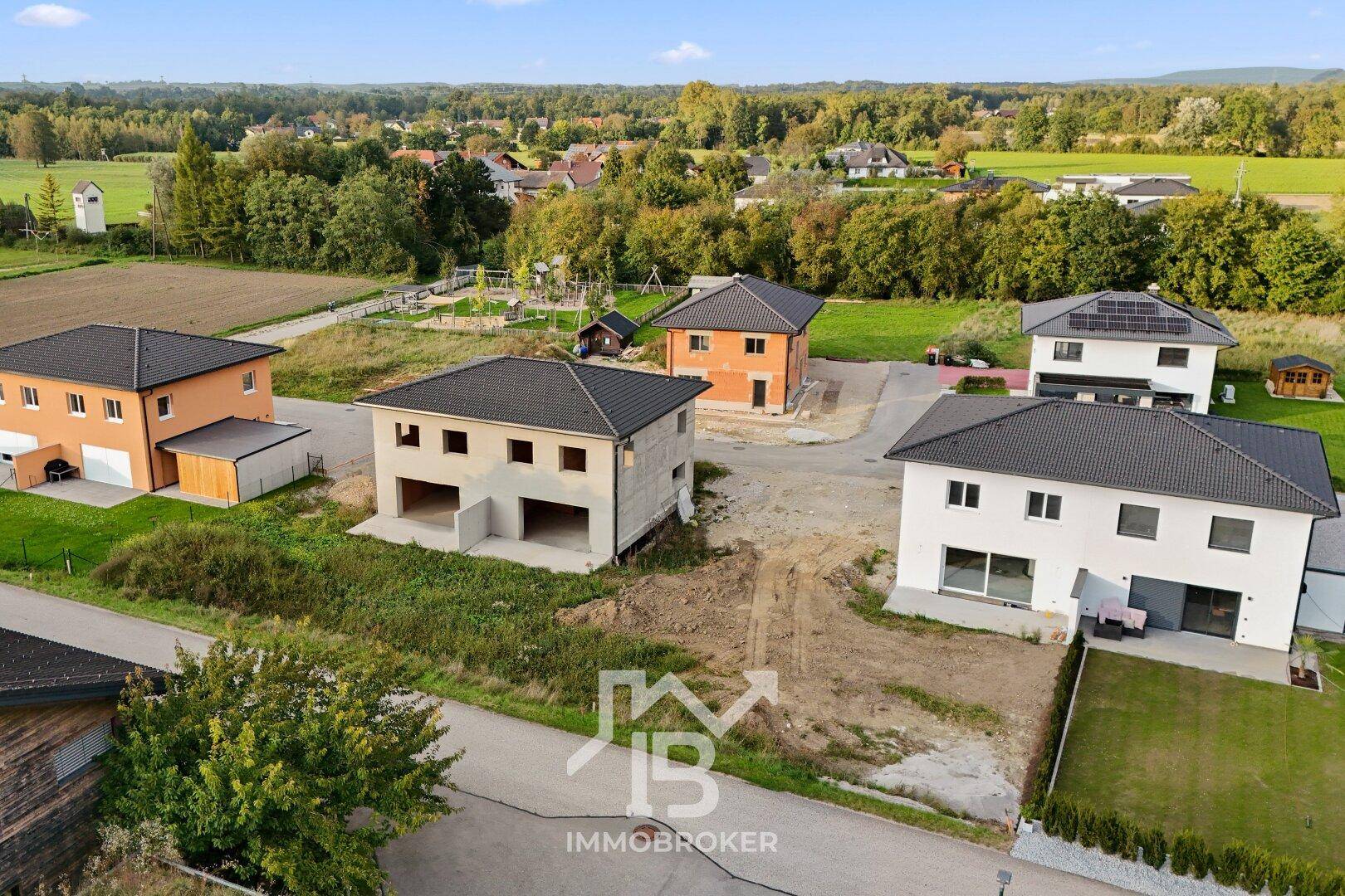 Luftaufnahme einer Neubausiedlung mit Häusern in verschiedenen Bauphasen und ländlicher Umgebung.