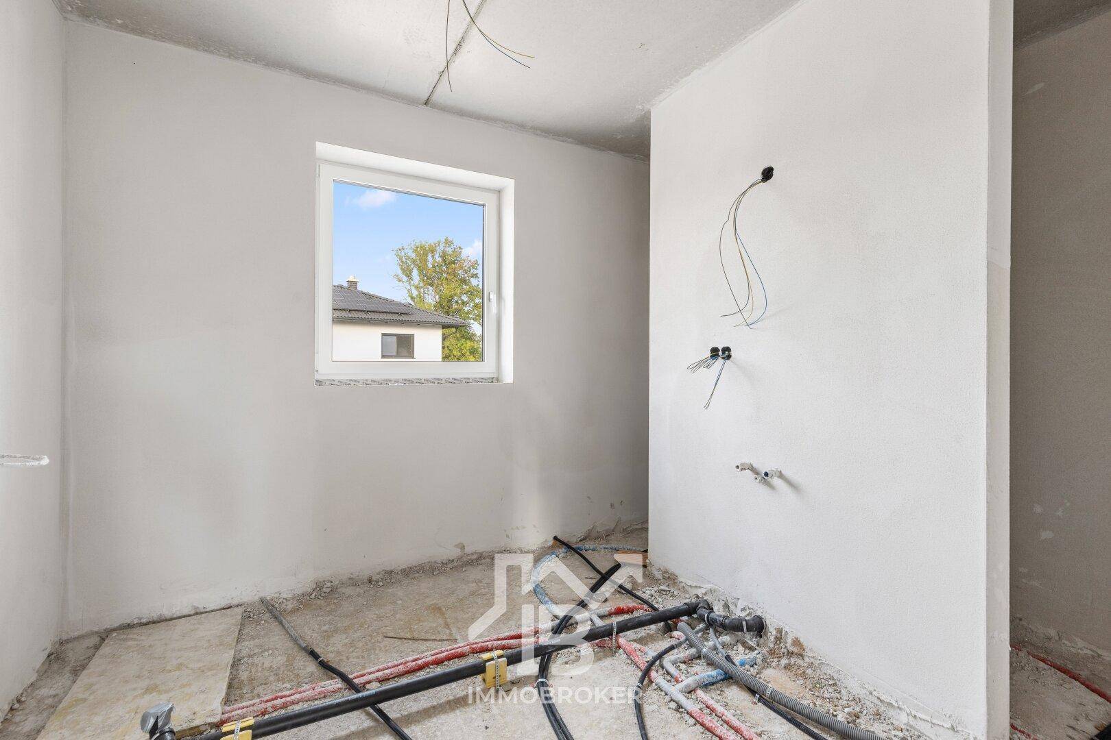 Rohbau eines Badezimmers mit Fenster und vorbereiteten Anschlüssen für Sanitärinstallationen.