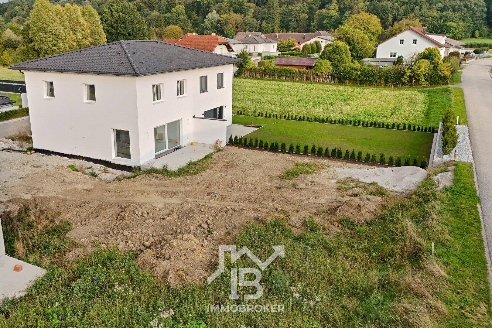 Fertiggestelltes weißes Haus mit neu angelegtem Rasen und Hecken, umgeben von ländlicher Landschaft.