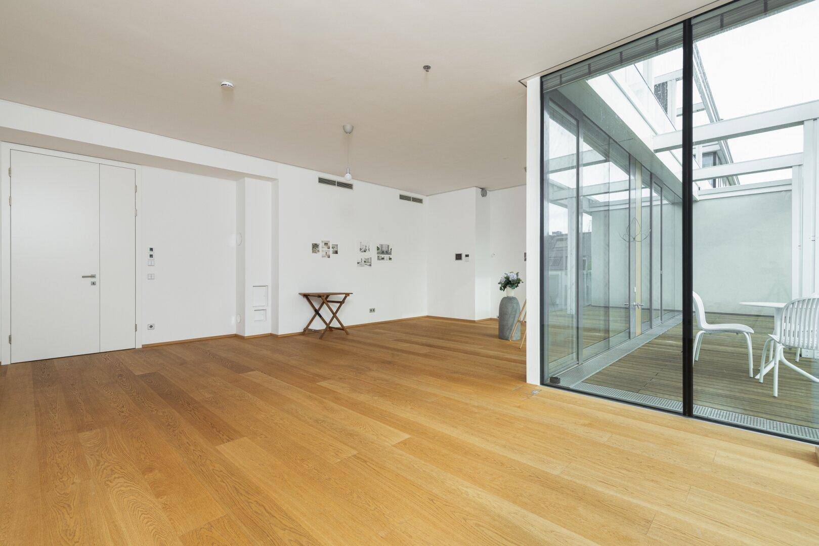 Weitläufiger Wohnbereich mit hellem Holzboden und großen Glasfronten, die zur Terrasse führen.