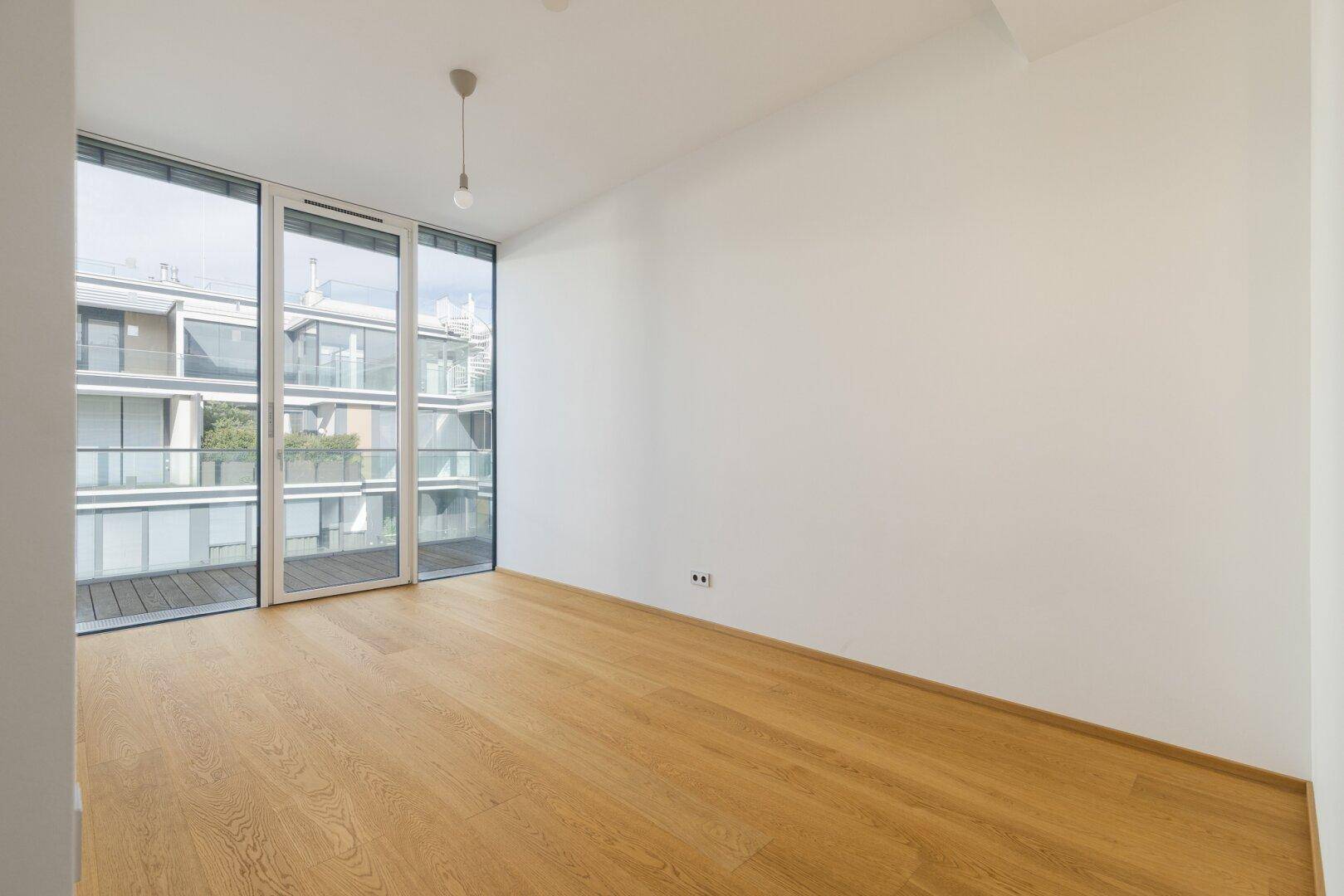 Heller, unmöblierter Raum mit Holzboden und großen Fenstern, ideal als Schlaf- oder Arbeitszimmer.