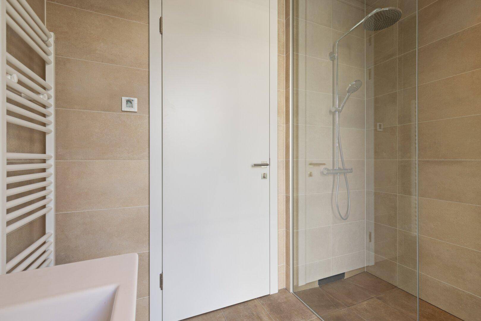 Helles Badezimmer mit großer, moderner Dusche, beigen Fliesen und beheiztem Handtuchhalter.