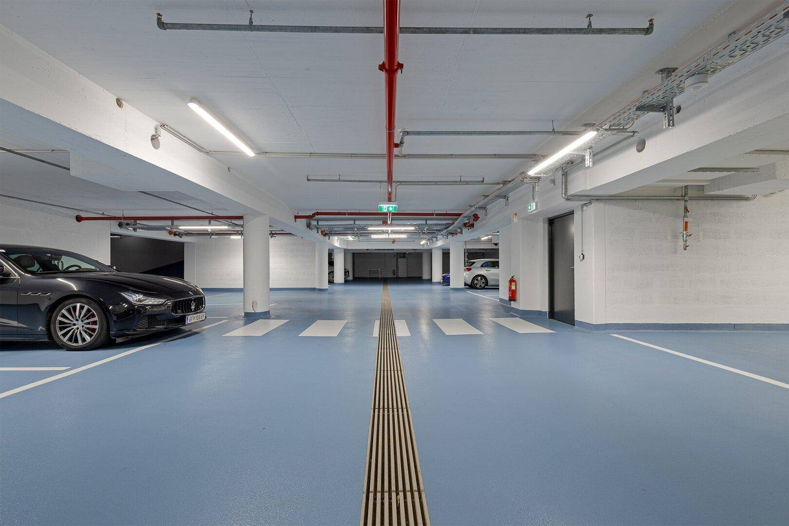 Geräumige Tiefgarage mit markierten Parkplätzen, moderner Beleuchtung und blauer Bodenmarkierung.