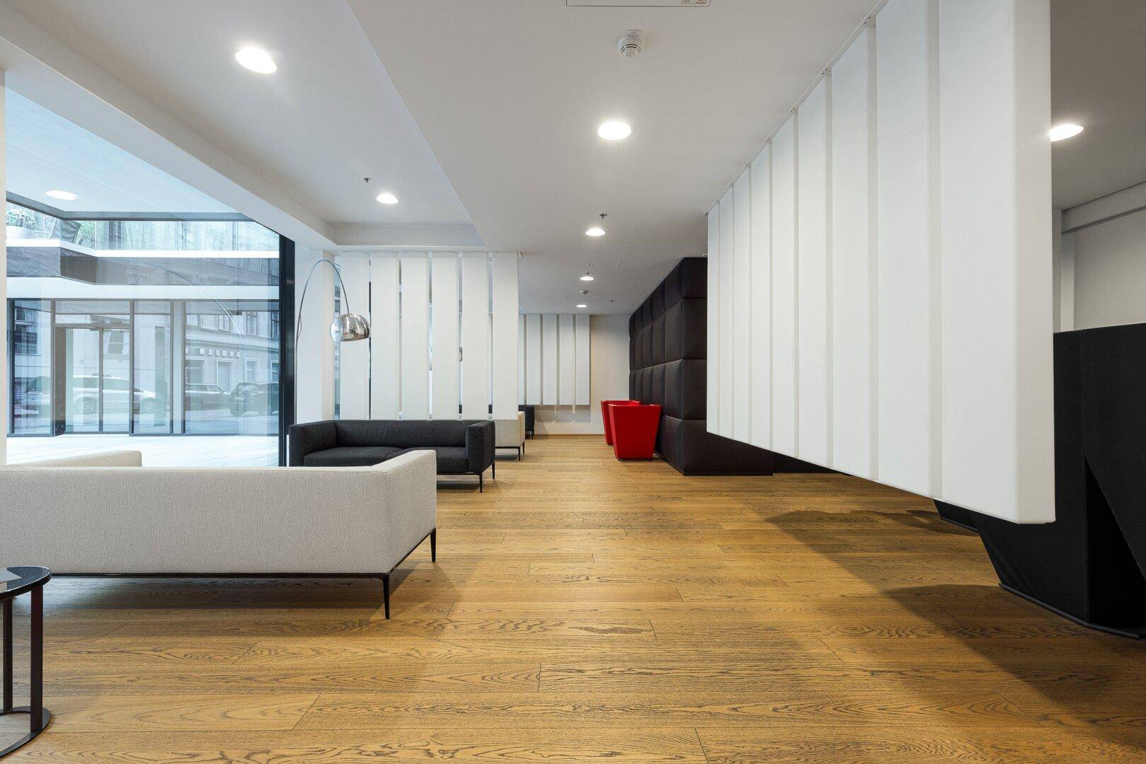 Stilvolle Gemeinschaftslounge mit modernen Sofas, Holzboden und viel Tageslicht.
