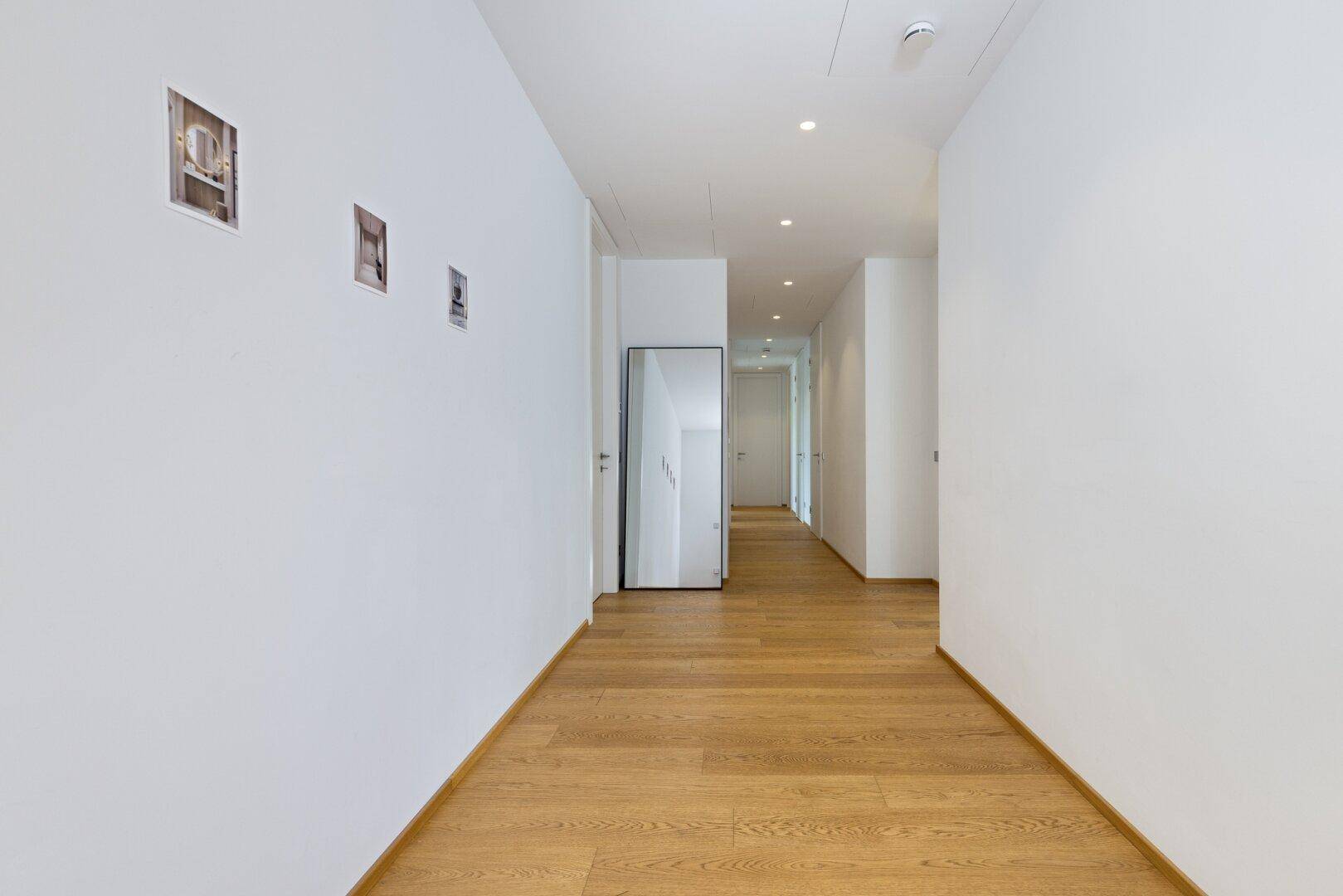 Langer, heller Flur mit Holzboden und minimalistischer Gestaltung, der zu den Zimmern führt.