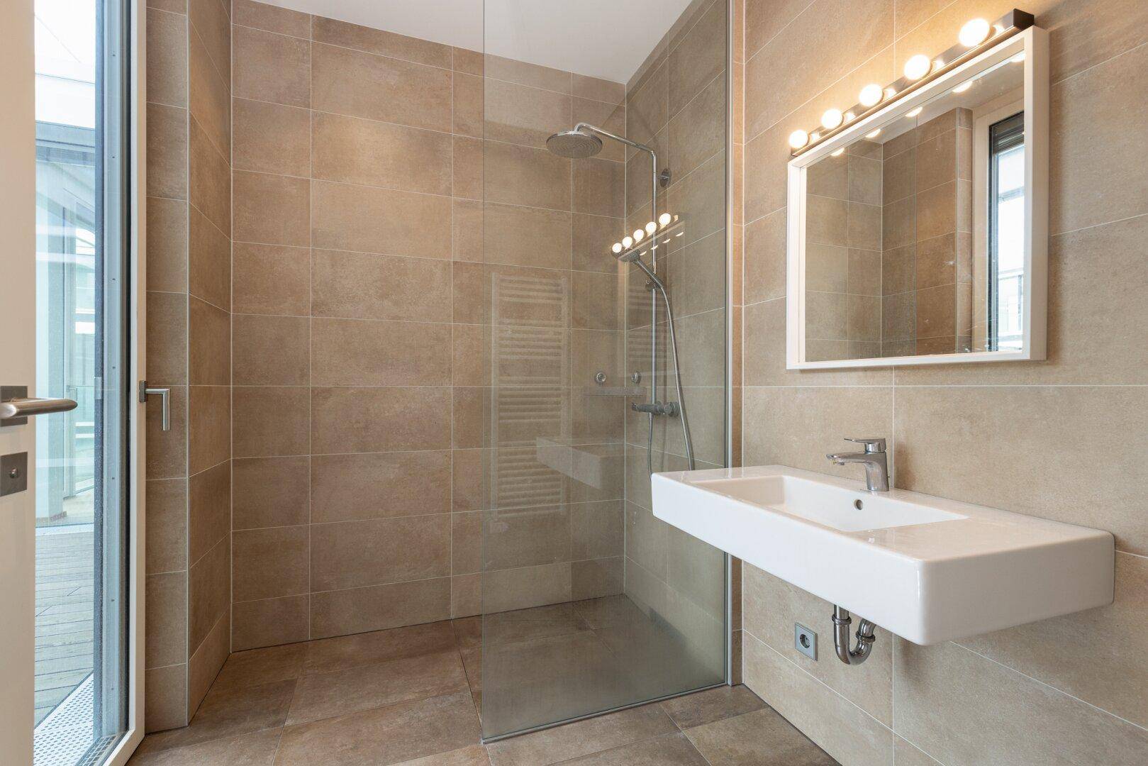 Modernes Badezimmer mit begehbarer Dusche, beigen Fliesen und einem schwebenden Waschbecken.