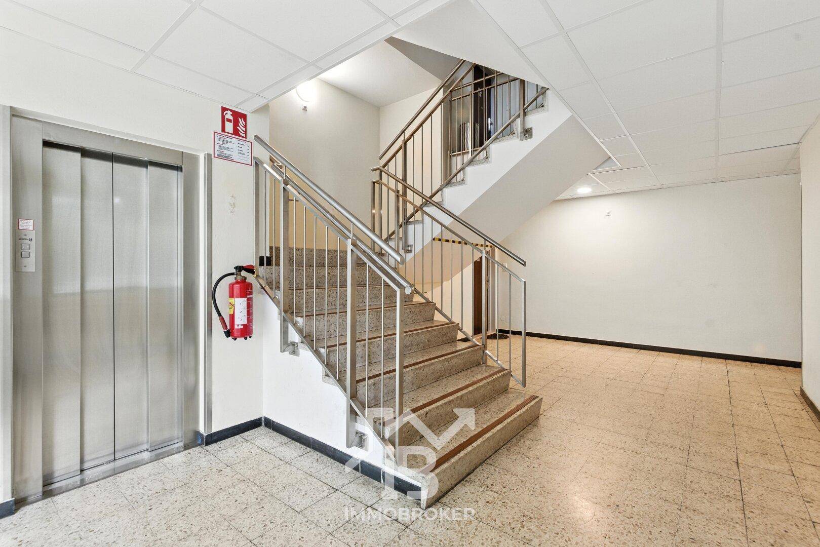 Treppenhaus mit Aufzug und Fliesenboden im Gemeinschaftsbereich des Gebäudes.