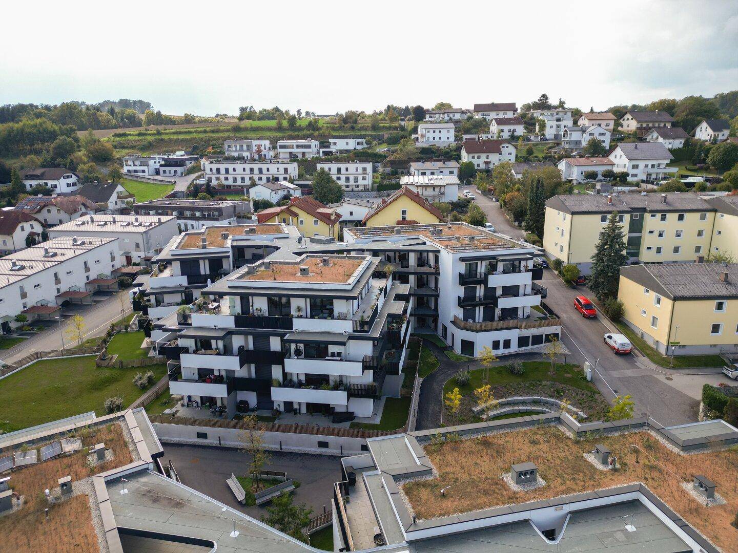 Luftaufnahme einer modernen Wohnanlage mit mehreren Gebäuden in einer grünen Hügellandschaft.