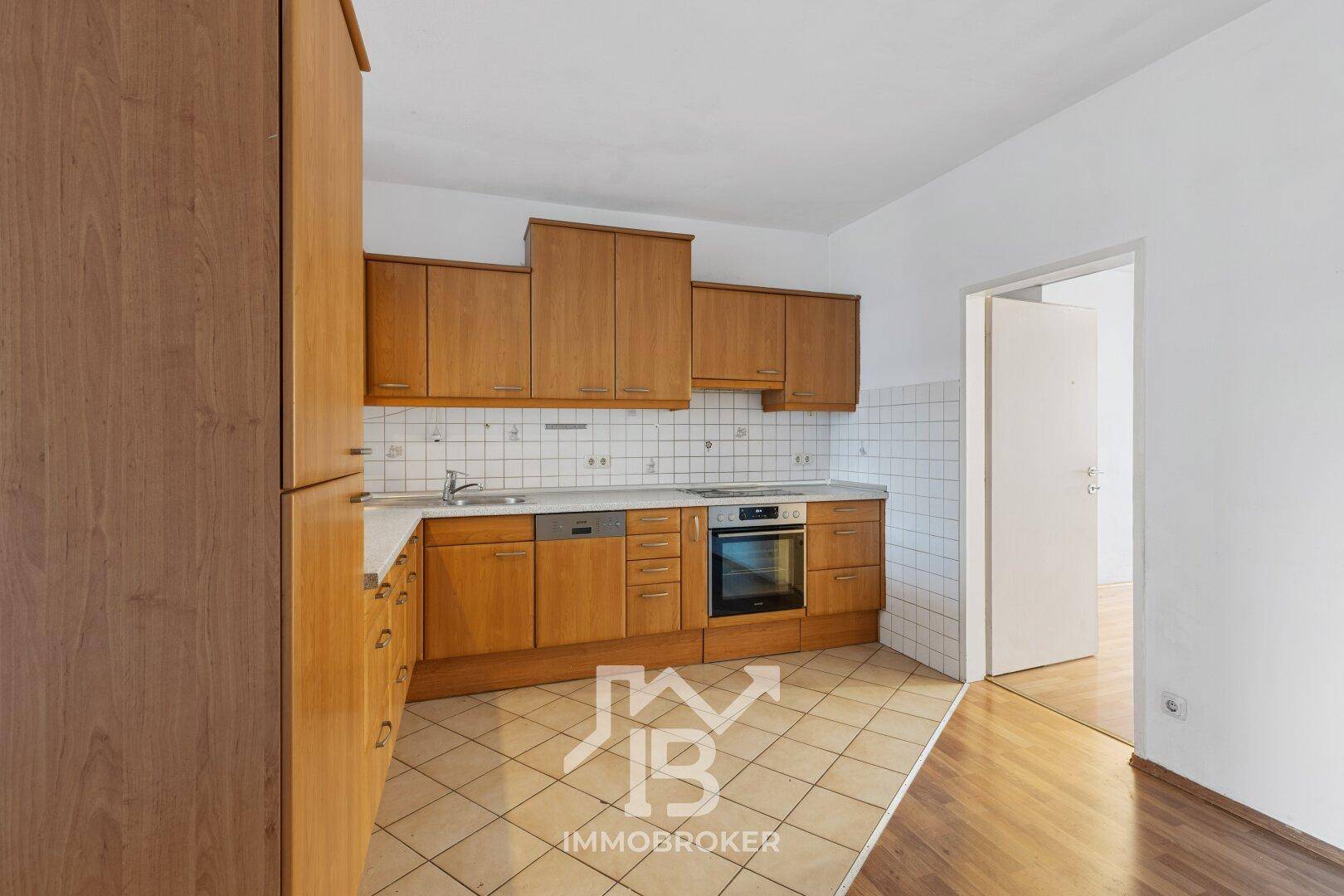 Küche mit Holzfronten, Fliesenboden und Zugang zu einem angrenzenden Raum.
