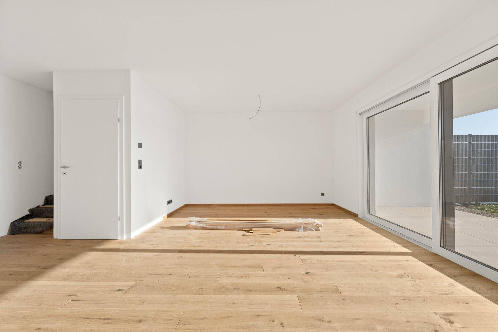 Geräumiges, helles Zimmer mit großen Schiebetüren und Holzplankenboden, ideal für einen Wohnbereich.
