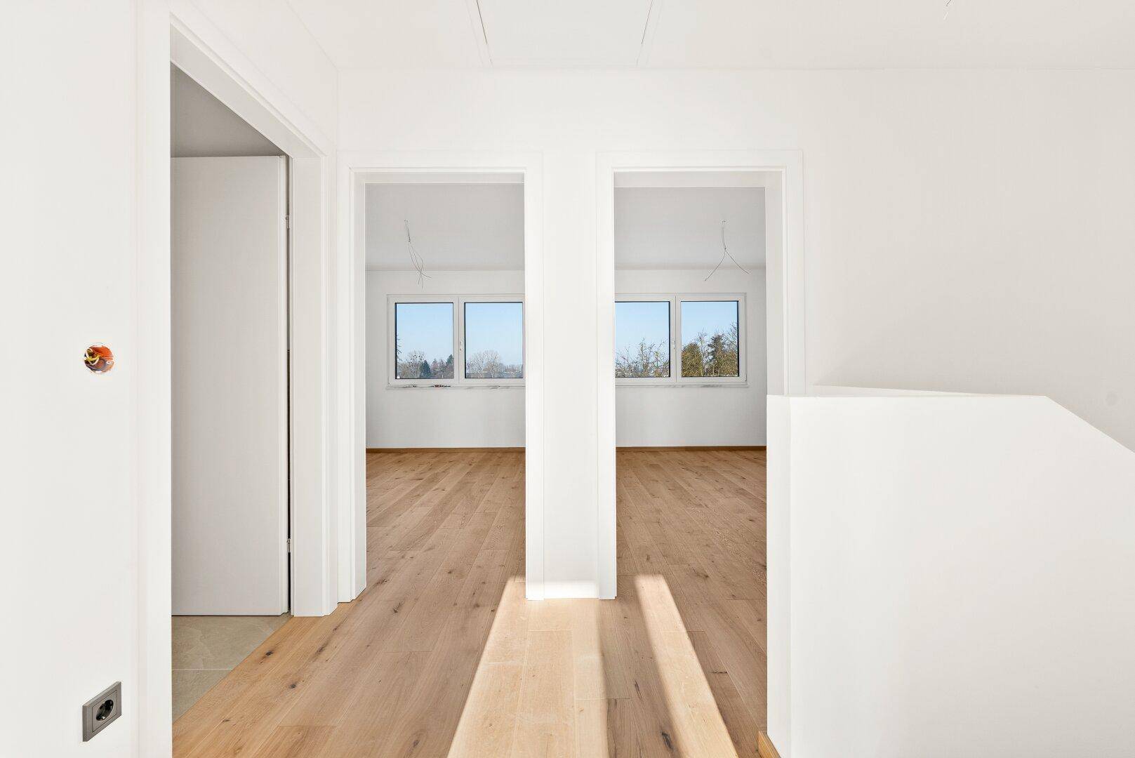 Heller Flur mit Holzplankenboden, der zu weiteren Zimmern mit großen Fenstern und Grünblick führt.