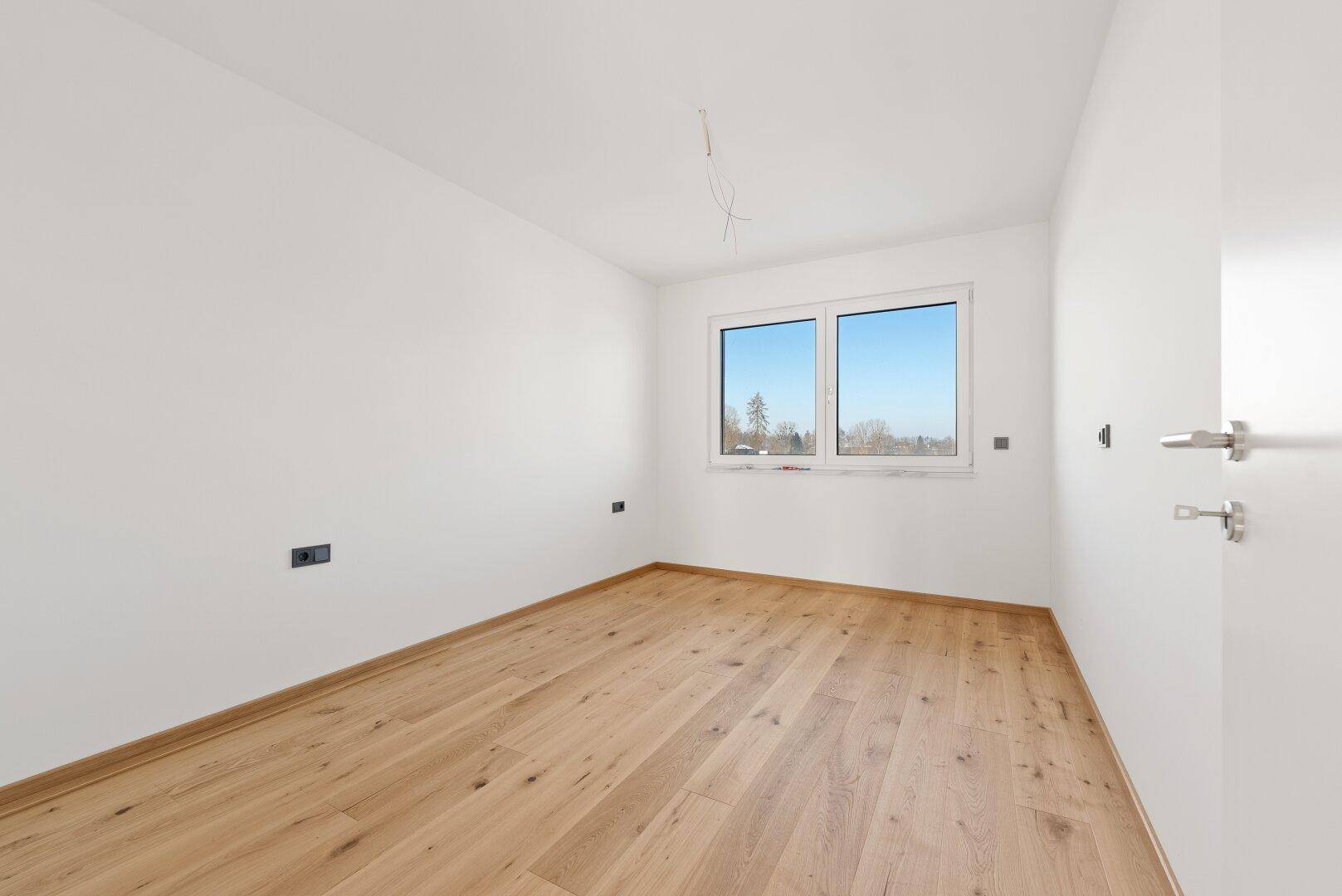 Helles Schlafzimmer mit Holzplankenboden und einem Fenster, das viel Tageslicht hereinlässt.