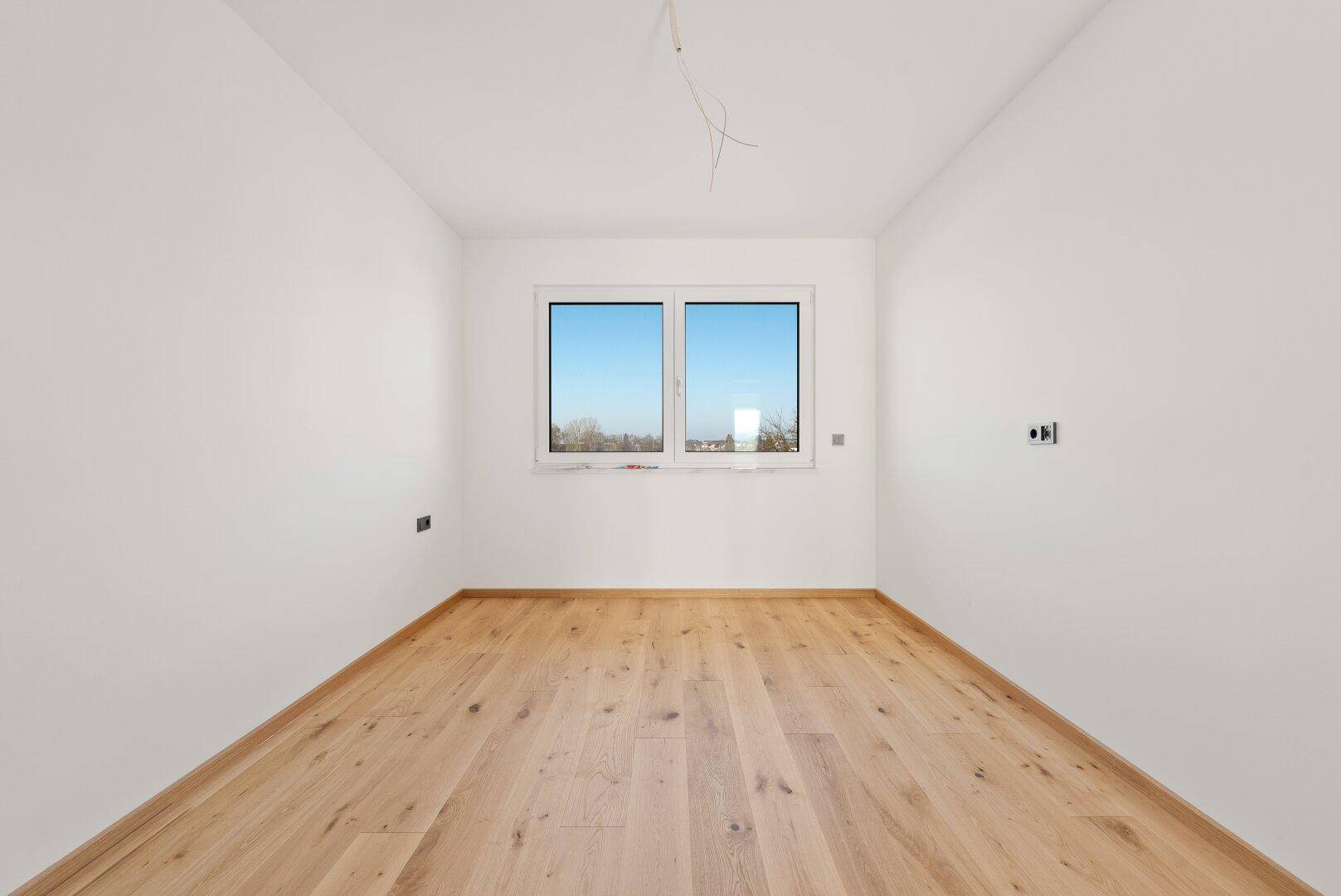 Leeres Schlafzimmer mit Holzboden und einem großen Fenster, das eine weite Aussicht bietet.