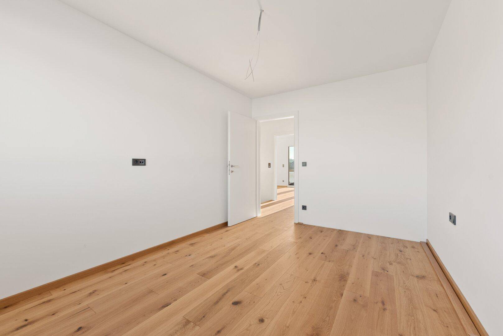 Helles Zimmer mit Parkettboden und einer Tür, die zu einem weiteren Bereich führt.