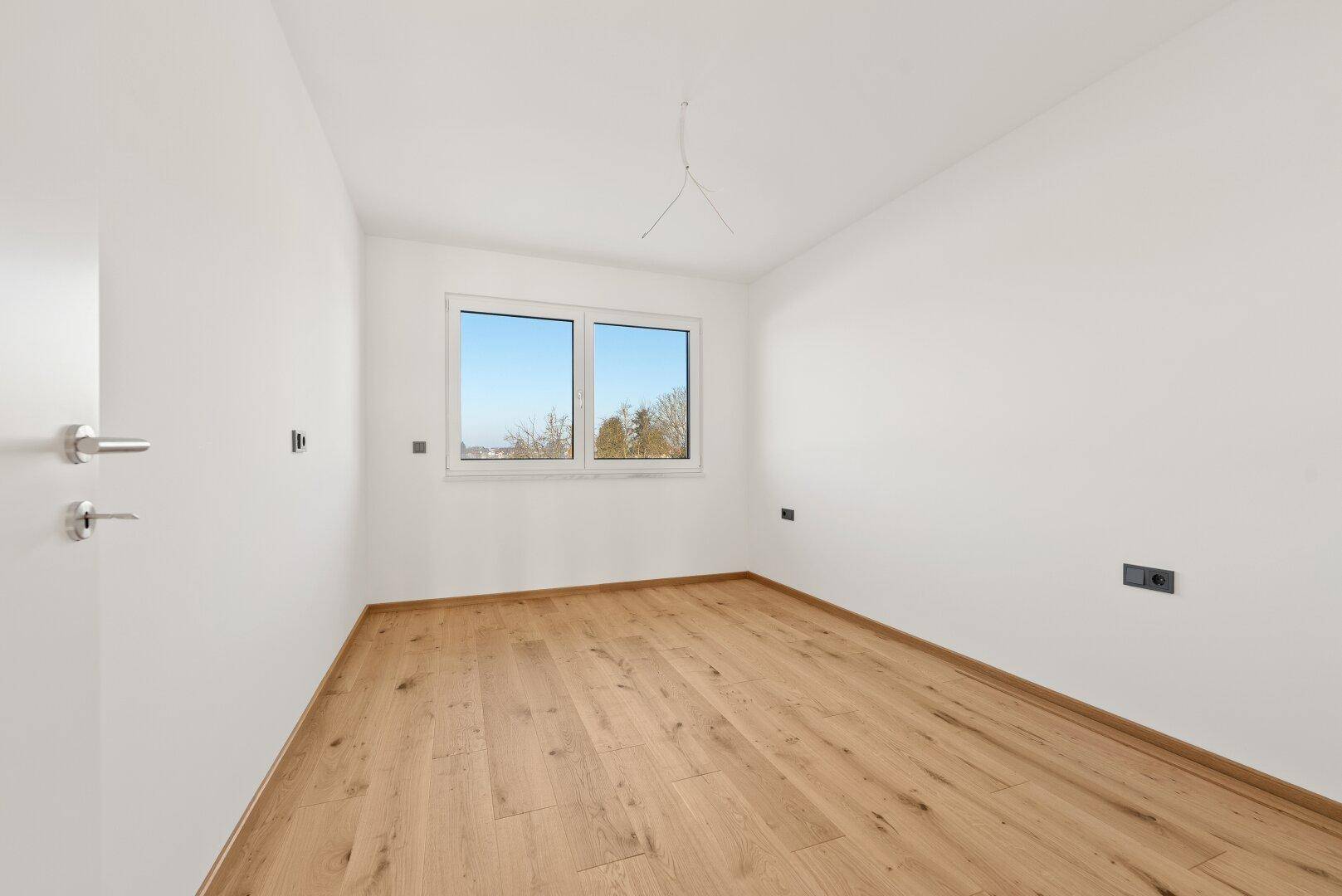 Gemütliches Schlafzimmer mit hellem Parkettboden und einem Fenster, das einen grünen Ausblick bietet.