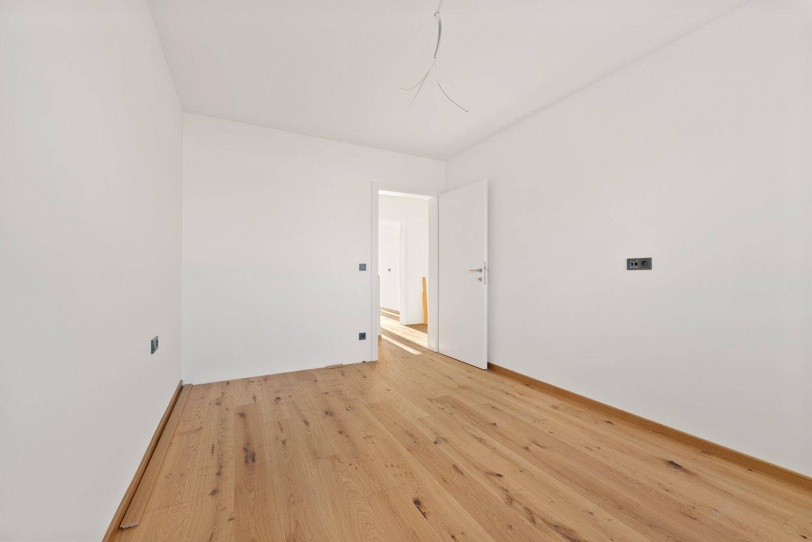 Helles Schlafzimmer mit Holzboden und einer Tür, die zu einem weiteren Raum führt.