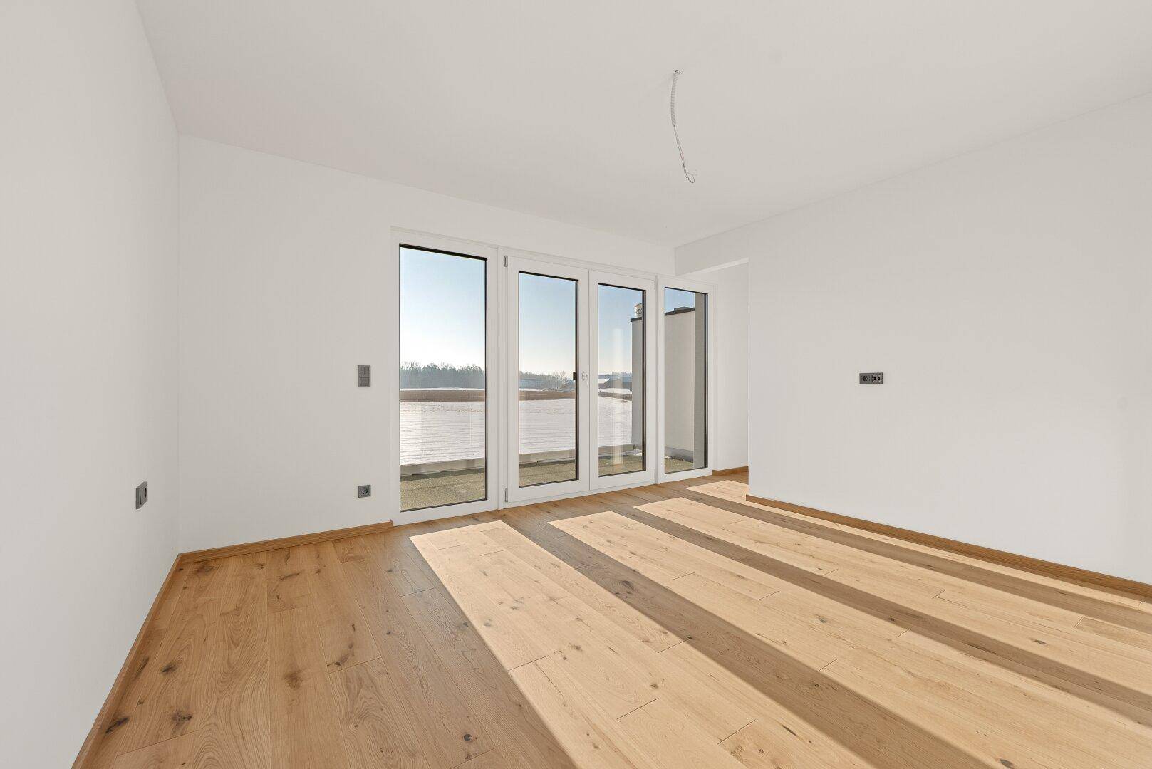 Geräumiger Raum mit hellem Parkett und einer großen Fensterfront, die viel Sonnenlicht einfängt.