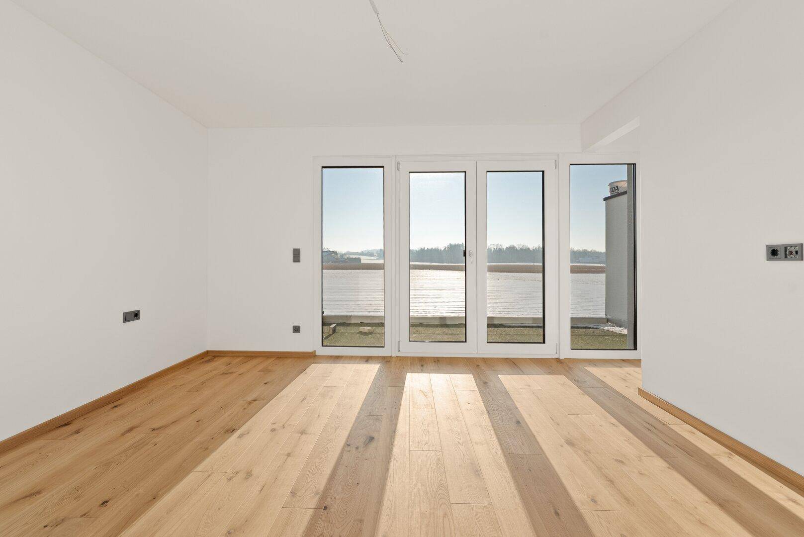Heller Wohnraum mit Parkettboden und einer breiten Glasfront, die einen weiten Blick ermöglicht.