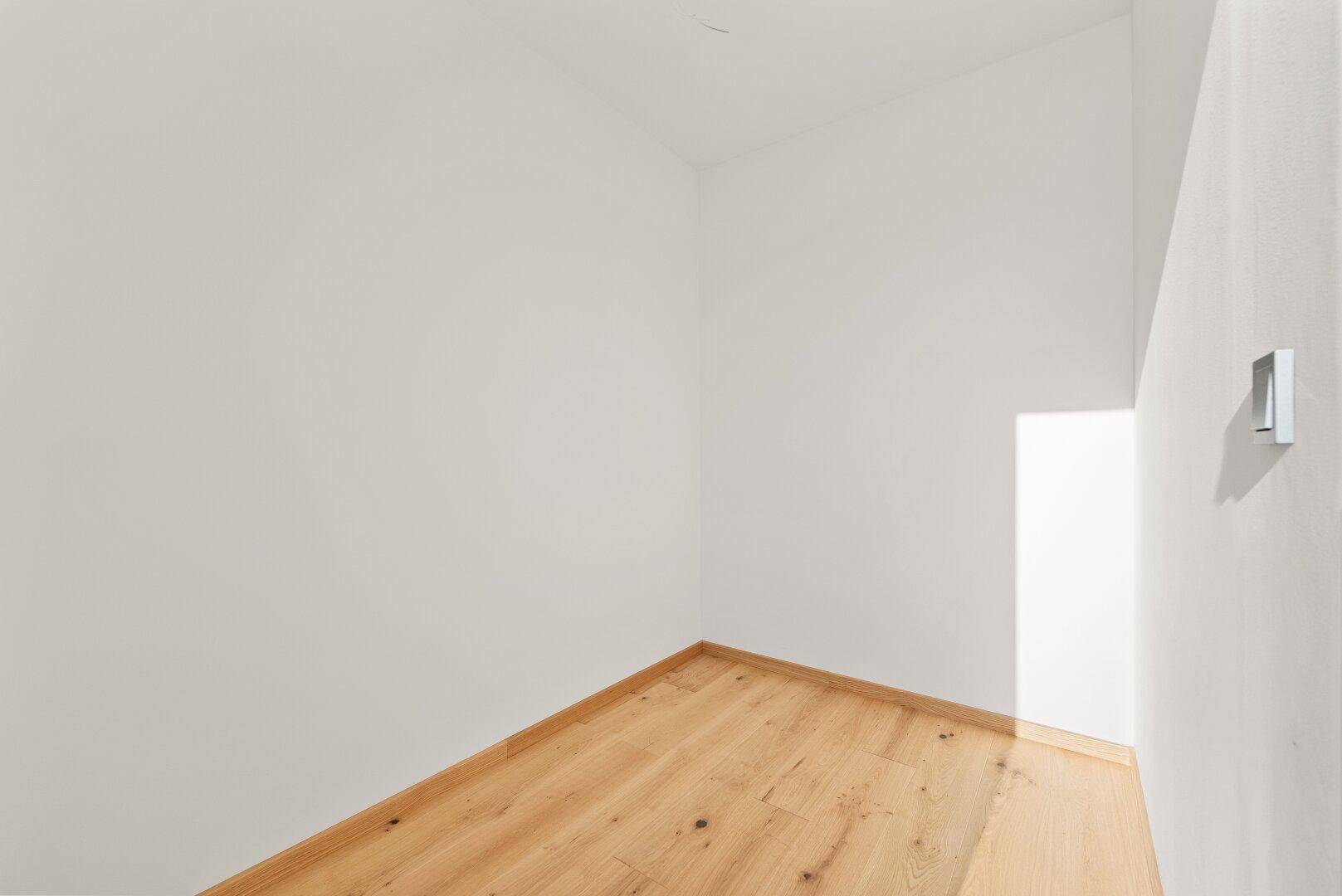 Kleiner, heller Eckbereich mit Holzboden und weißen Wänden, ideal als Abstellfläche.