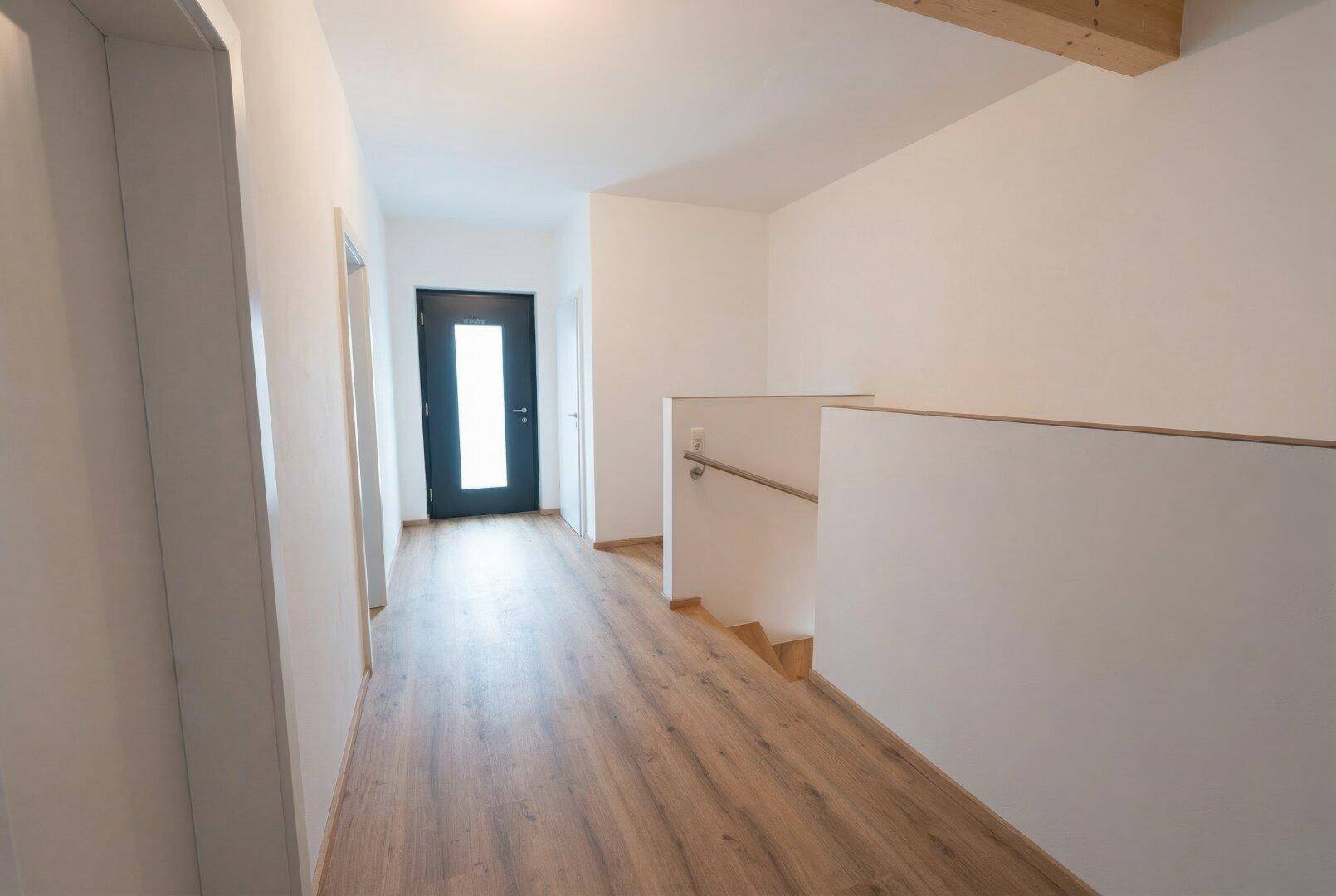 Heller Flur mit Holzboden, weißen Wänden und moderner dunkler Eingangstür.