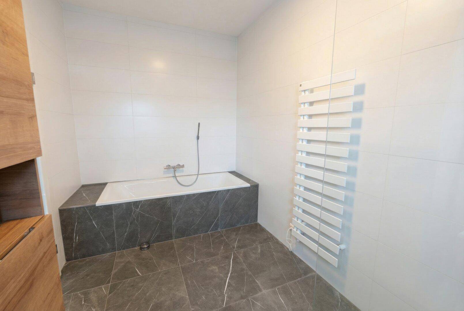 Modernes Badezimmer mit eingebauter Badewanne, Fliesenboden und beheiztem Handtuchhalter.