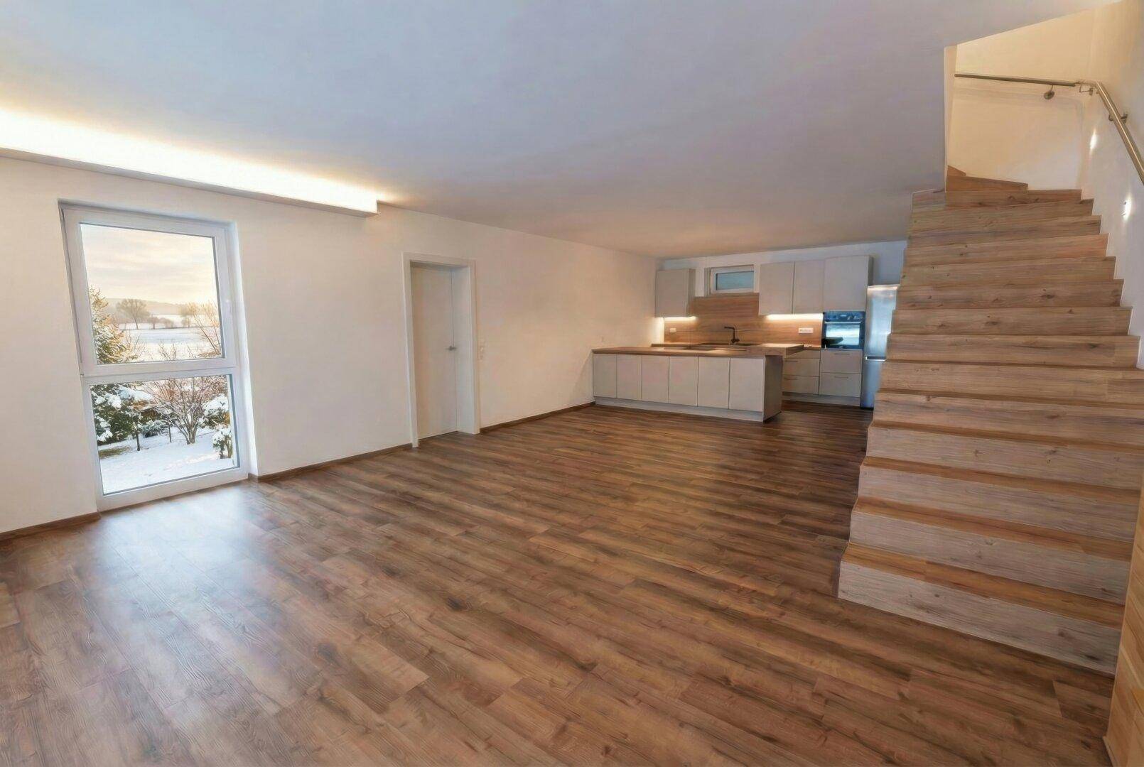 Offener Wohnbereich mit moderner Einbauküche, Holztreppe und Blick auf die verschneite Landschaft.